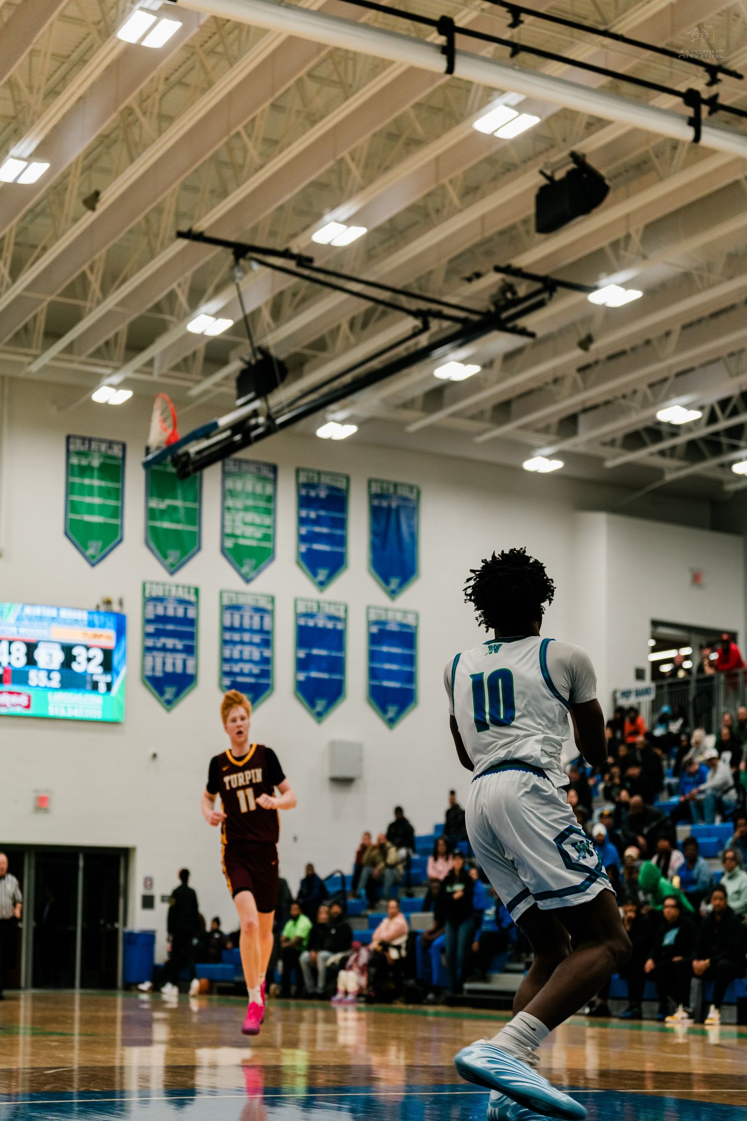 Player #10 in white runs downcourt as a maroon-uniformed opponent watches during a high school basketball game.