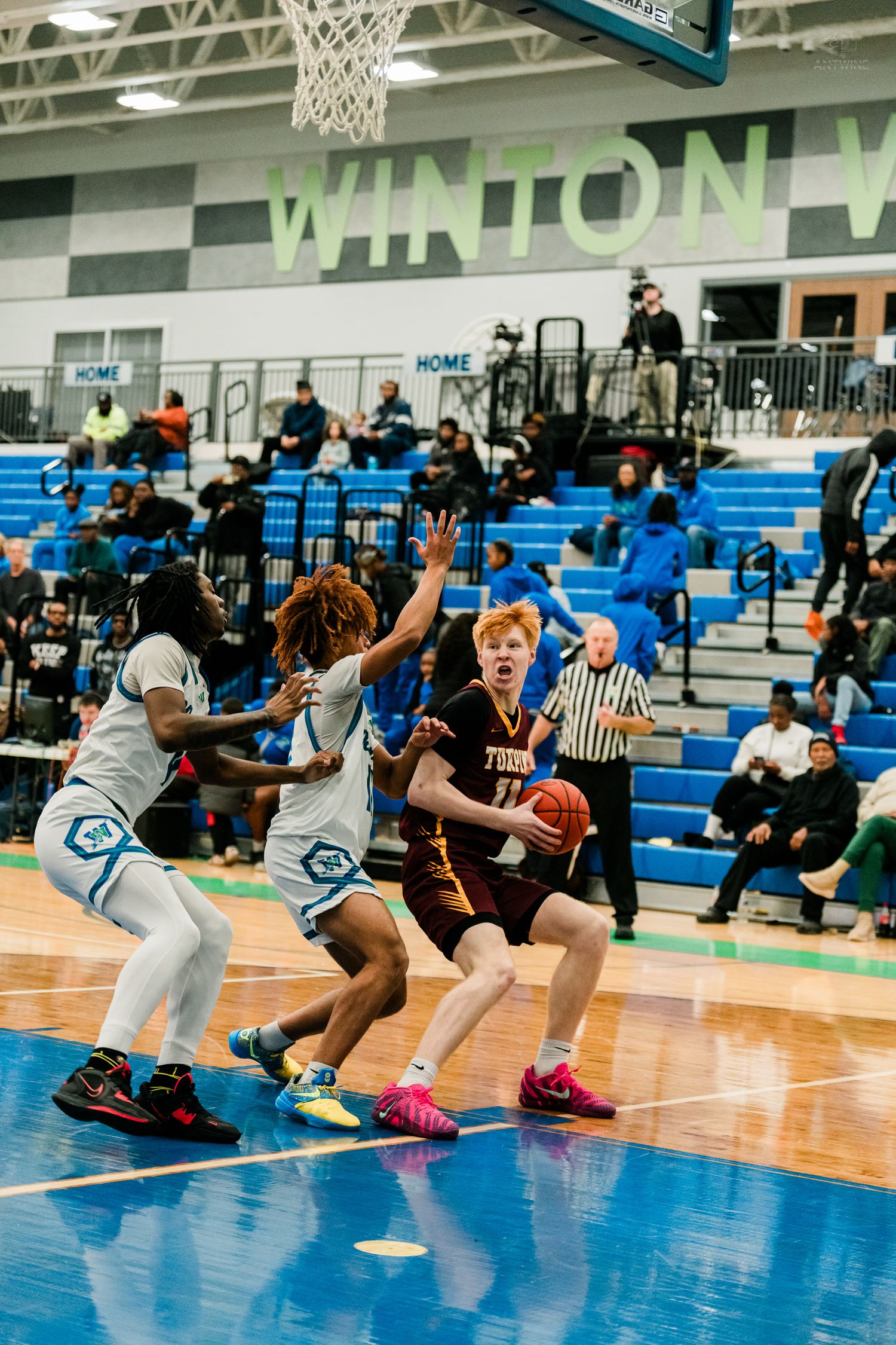 A redheaded player drives to the basket against two defenders during a high school basketball game at Winton Woods.