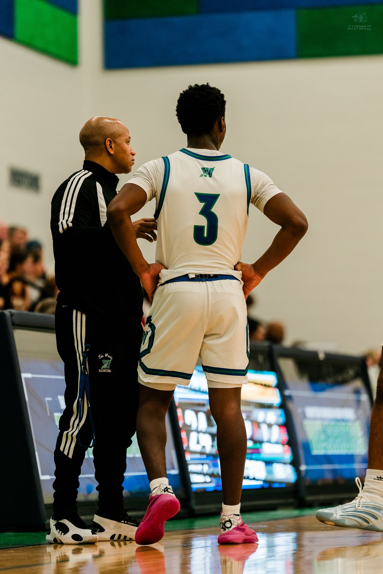 High school basketball coach gives instructions to player #3 in white Winton Woods uniform during game.