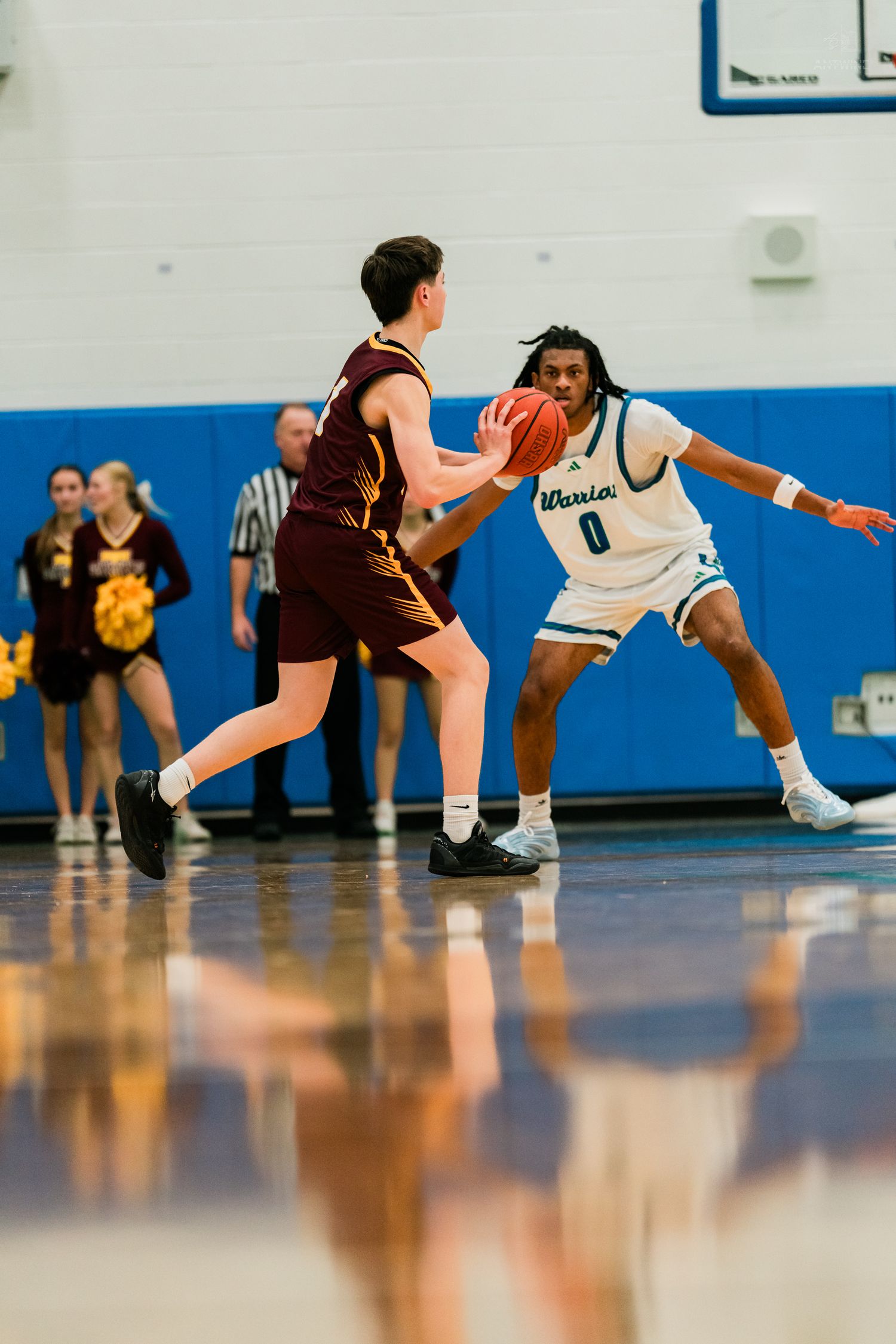 Warriors player number 0 in teal uniform plays defense against maroon-uniformed opponent on basketball court.
