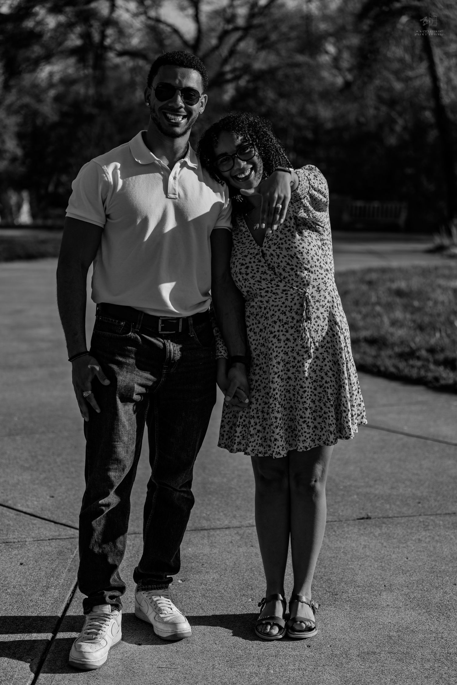 Black and white portrait of a happy couple posing together on a sunny park pathway.