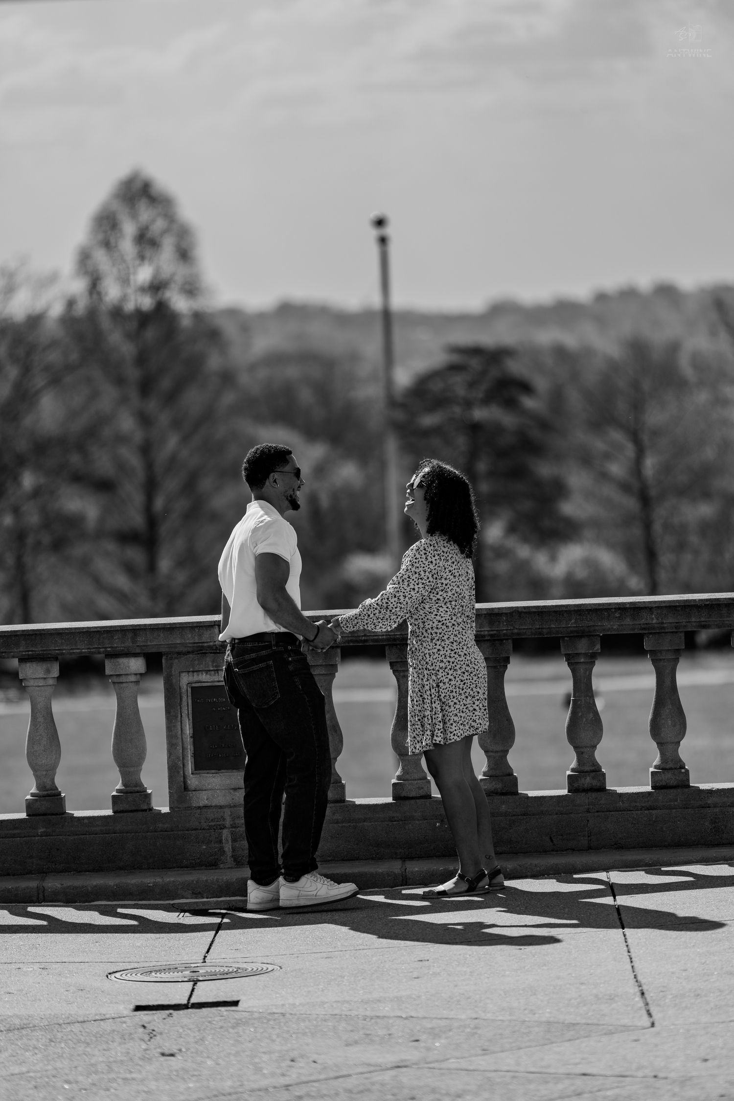 Black and white photo of couple holding hands on ornate stone balustrade terrace outdoors.