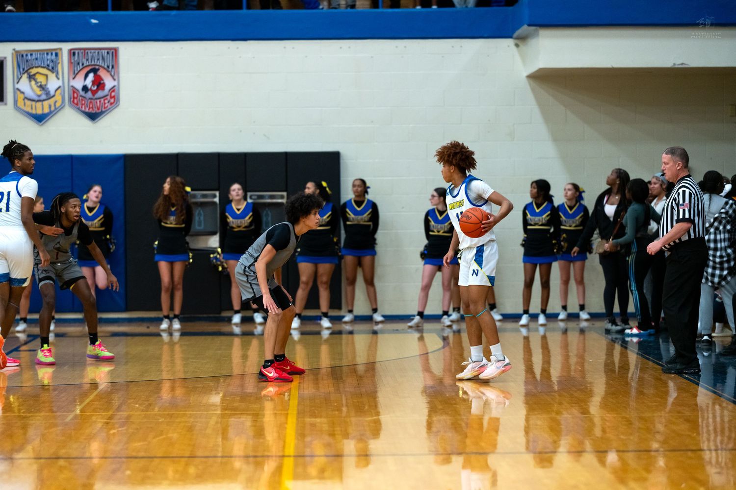 High school basketball player in blue uniform prepares free throw while cheerleaders line the baseline.