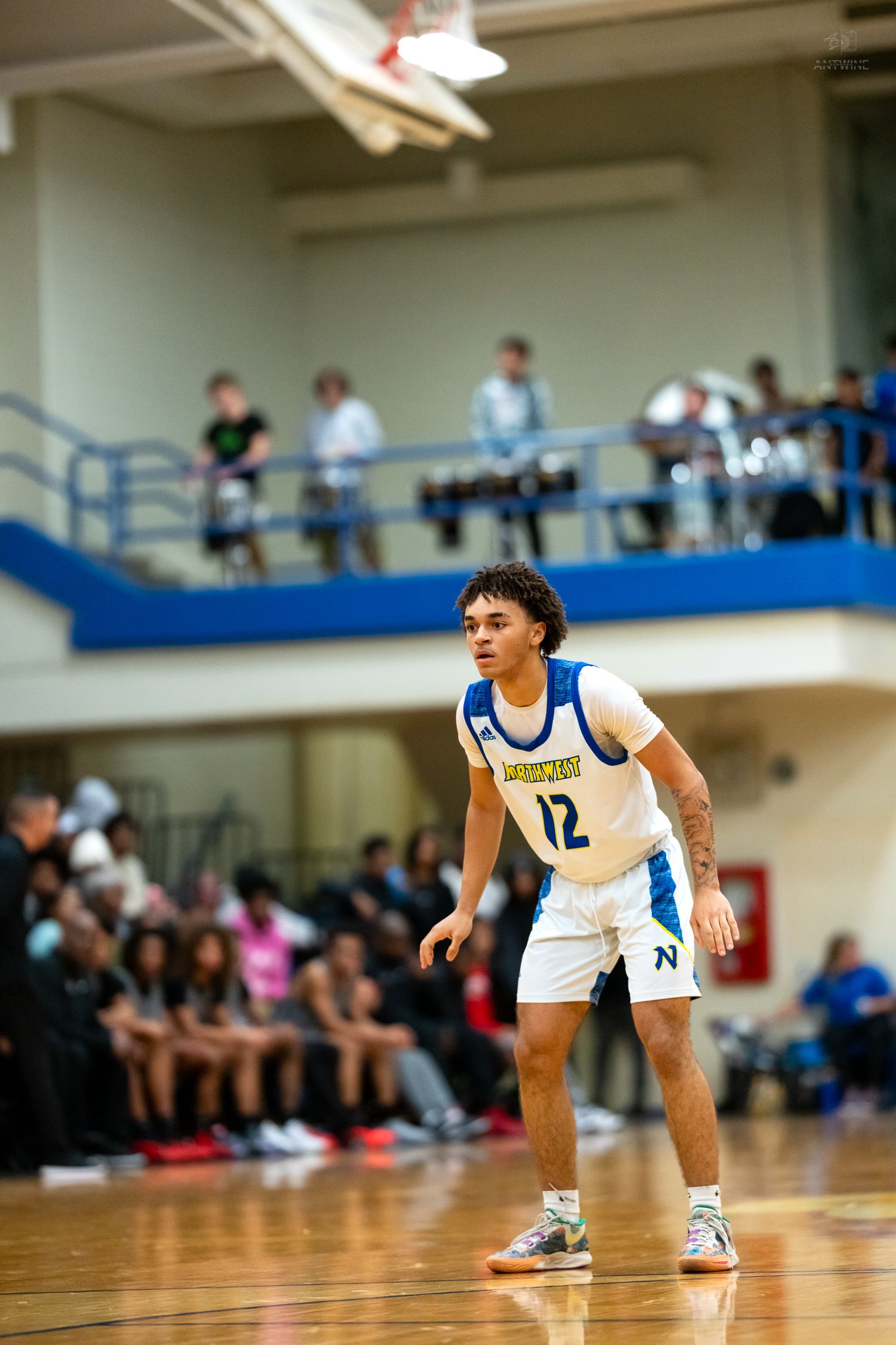 High school basketball player #12 in white uniform stands ready on court.