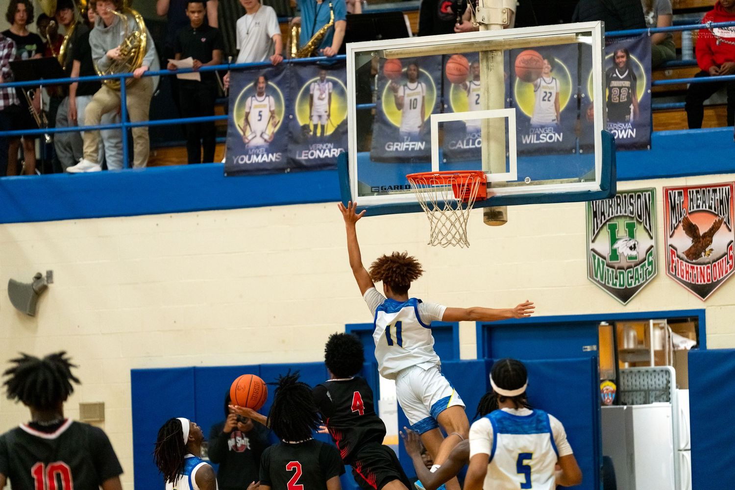 High school basketball player number 11 attempts a layup over defenders in a crowded gym.