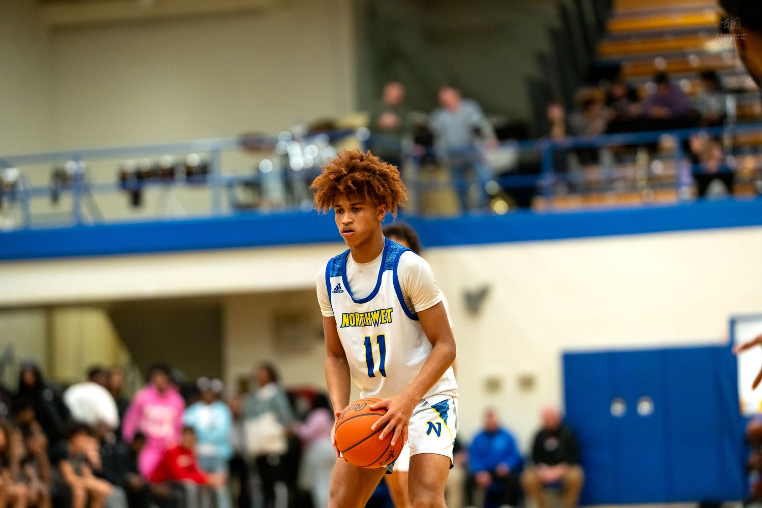 Young basketball player wearing number 11 jersey handles ball during high school game on indoor court.