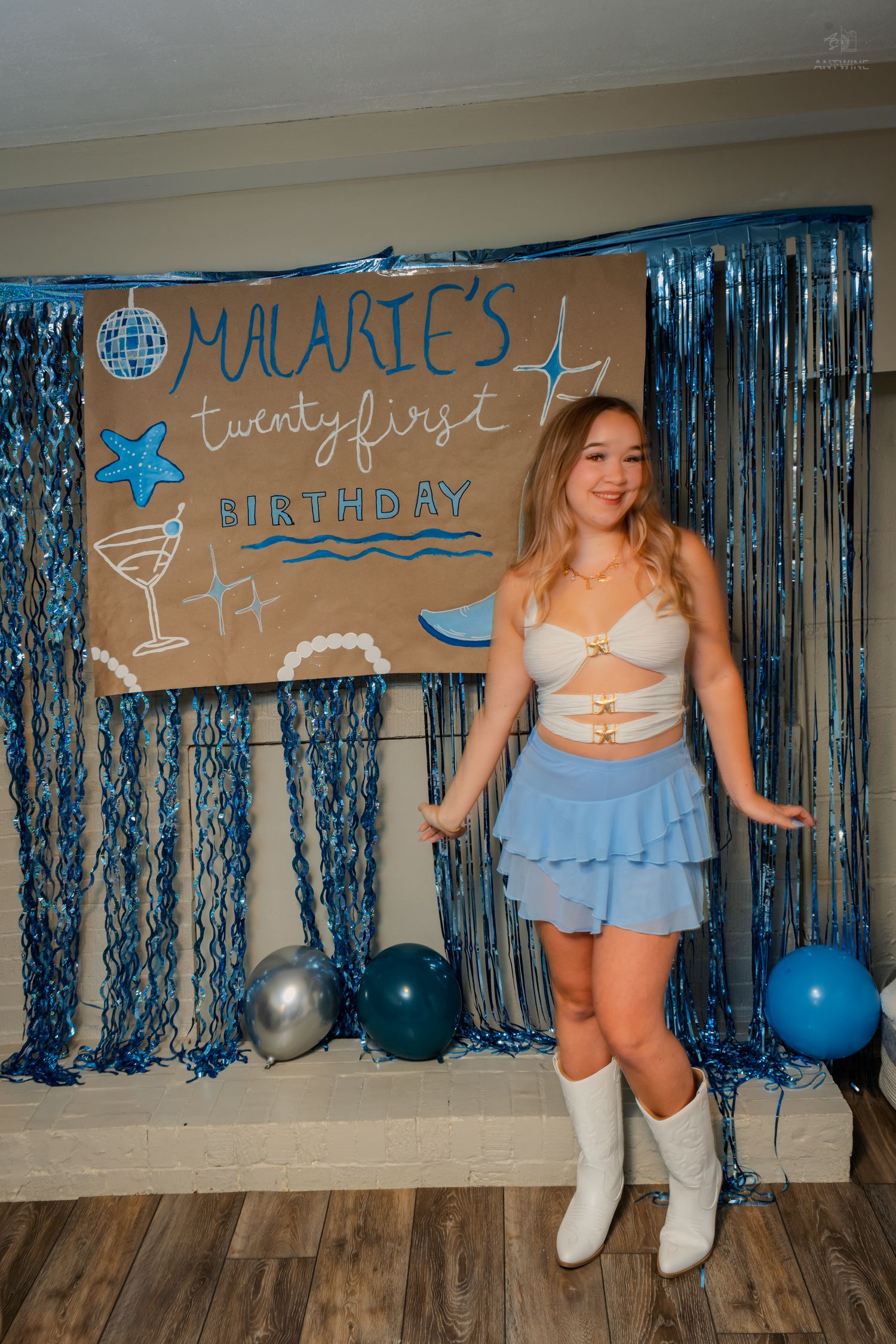 Woman in white boots and blue ruffle skirt posing at decorated 21st birthday party backdrop.
