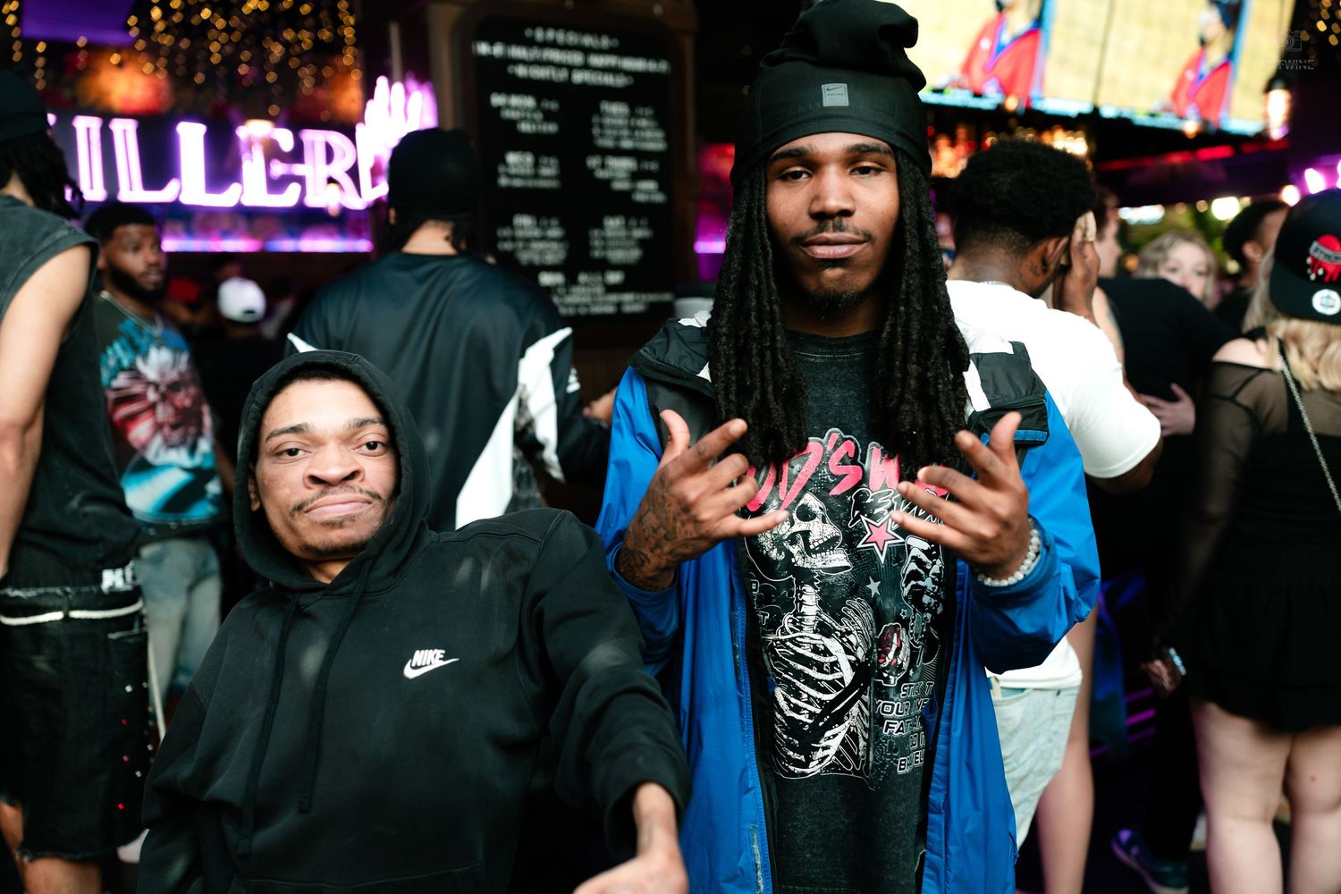 Two men posing together smiling at a lively neon-lit nightclub event.