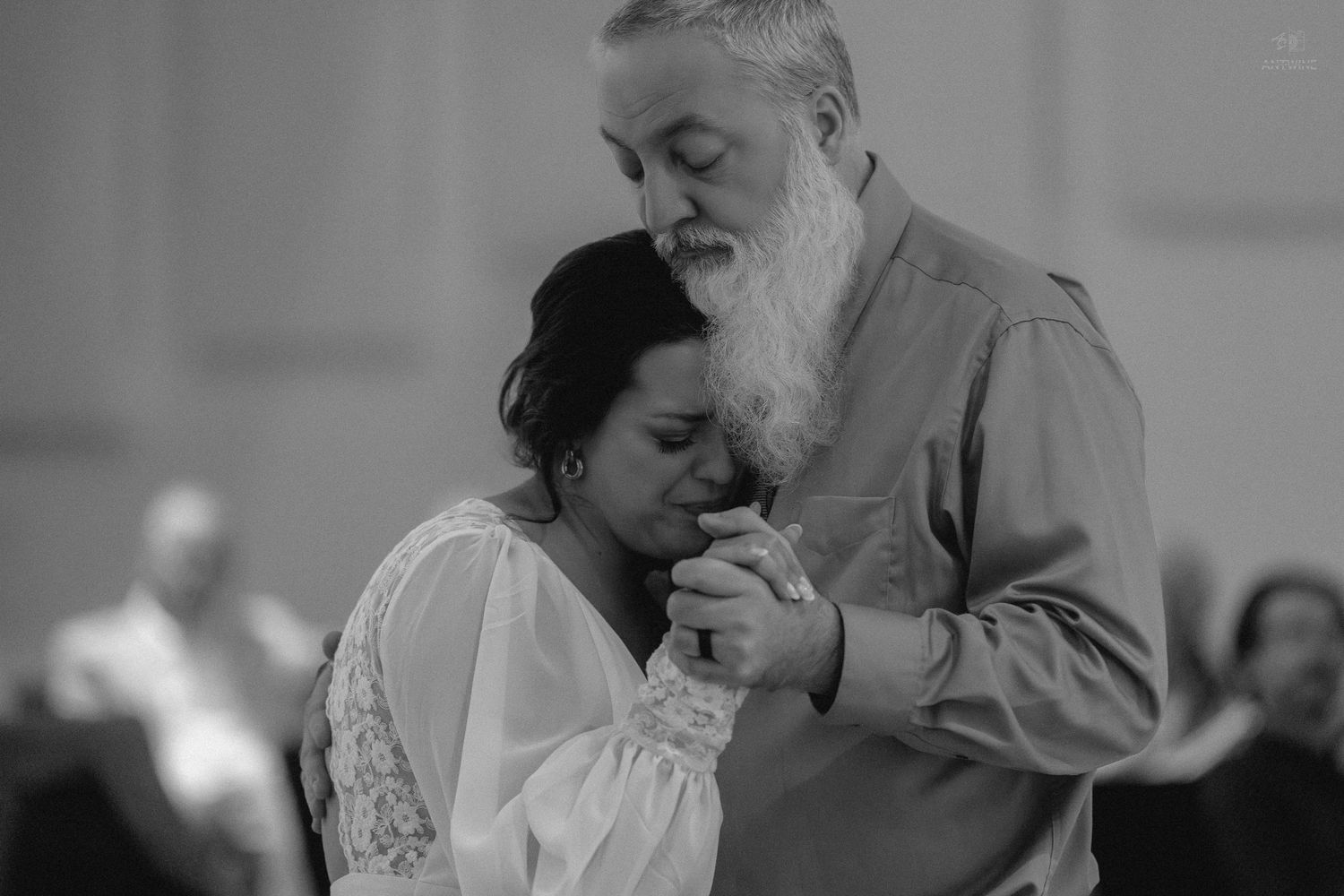 Black and white photo of a bride dancing emotionally with an older bearded man at a wedding.
