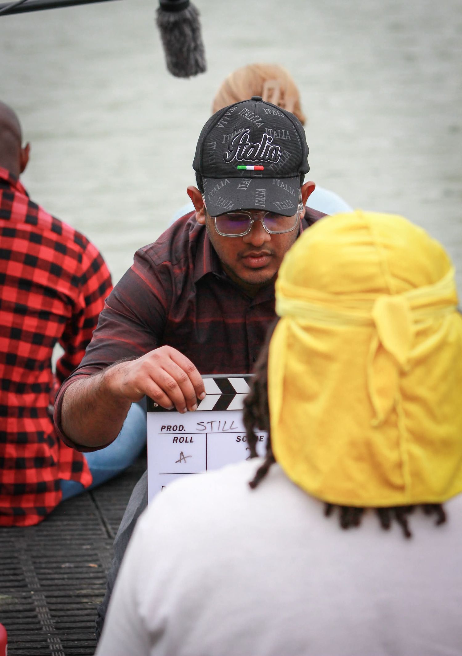 Film director holding clapperboard on movie set near water.