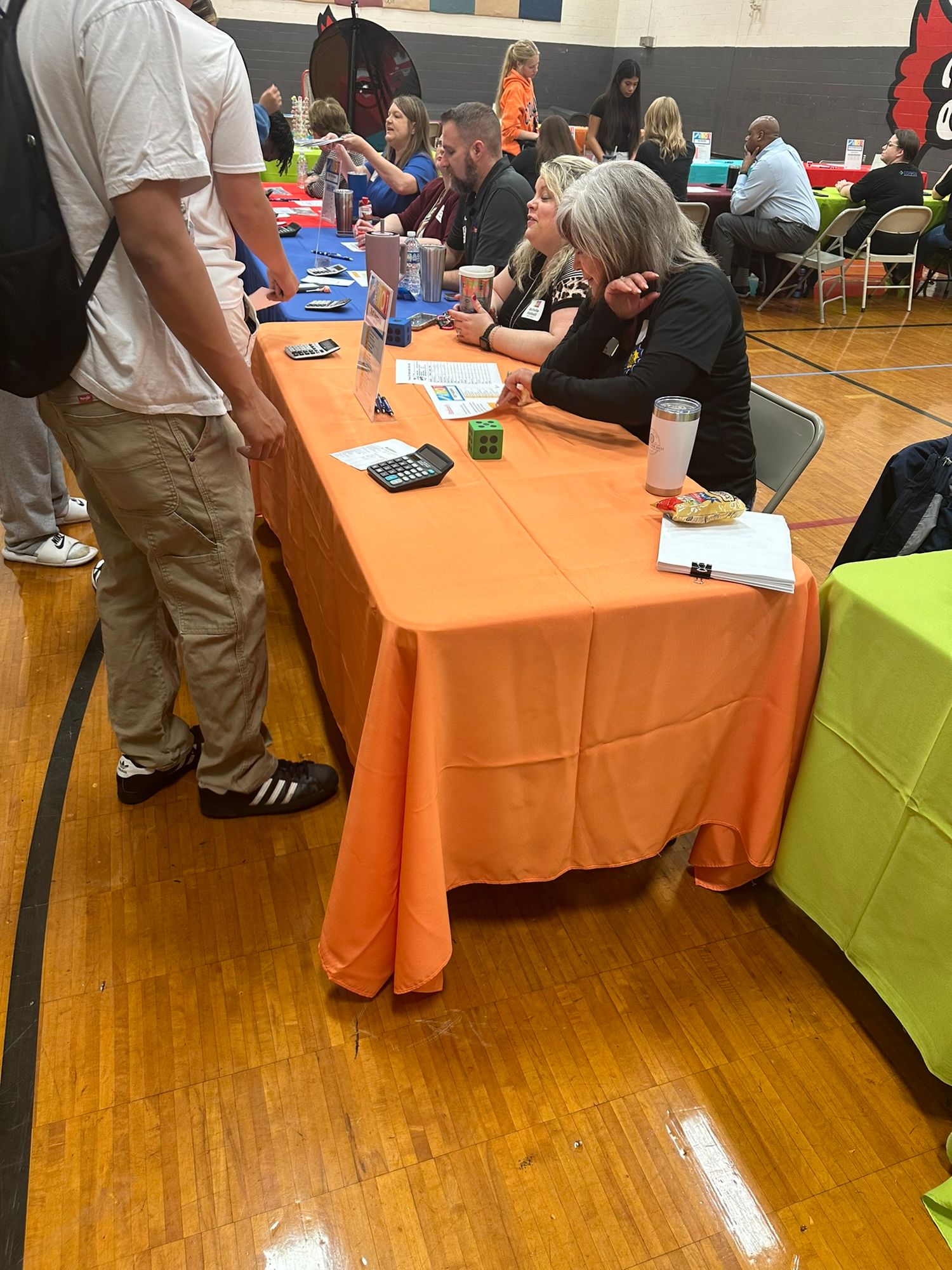 People networking at a job fair with orange tablecloth in a gymnasium.