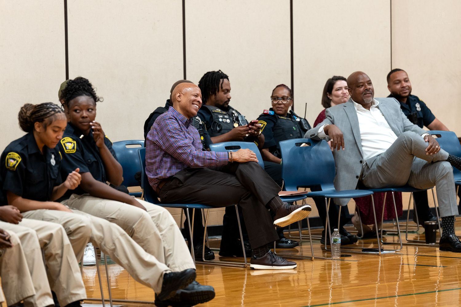 Diverse group of police officers and civilians seated in chairs at an indoor community meeting.