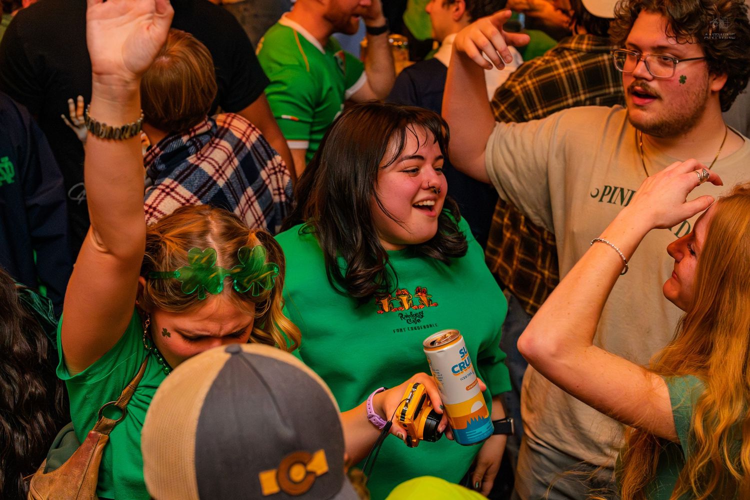 Cheerful woman in green St. Patrick's Day shirt laughing and celebrating with friends at a bar.