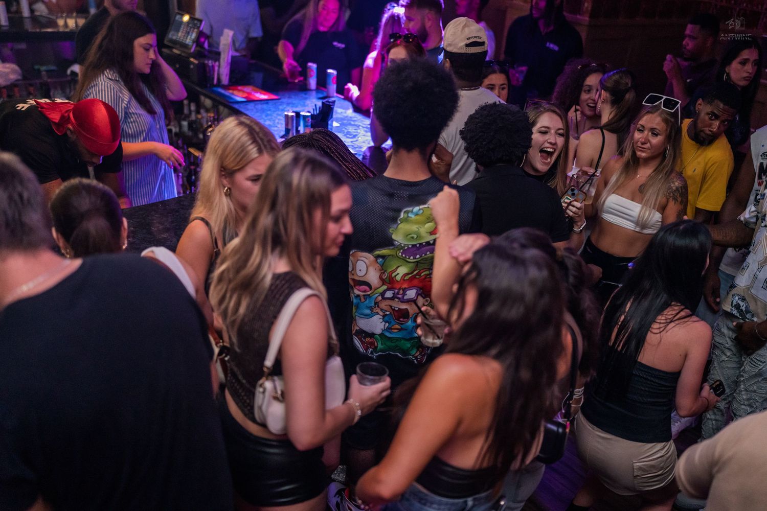 Group of young women laughing and socializing on a crowded nightclub dance floor.