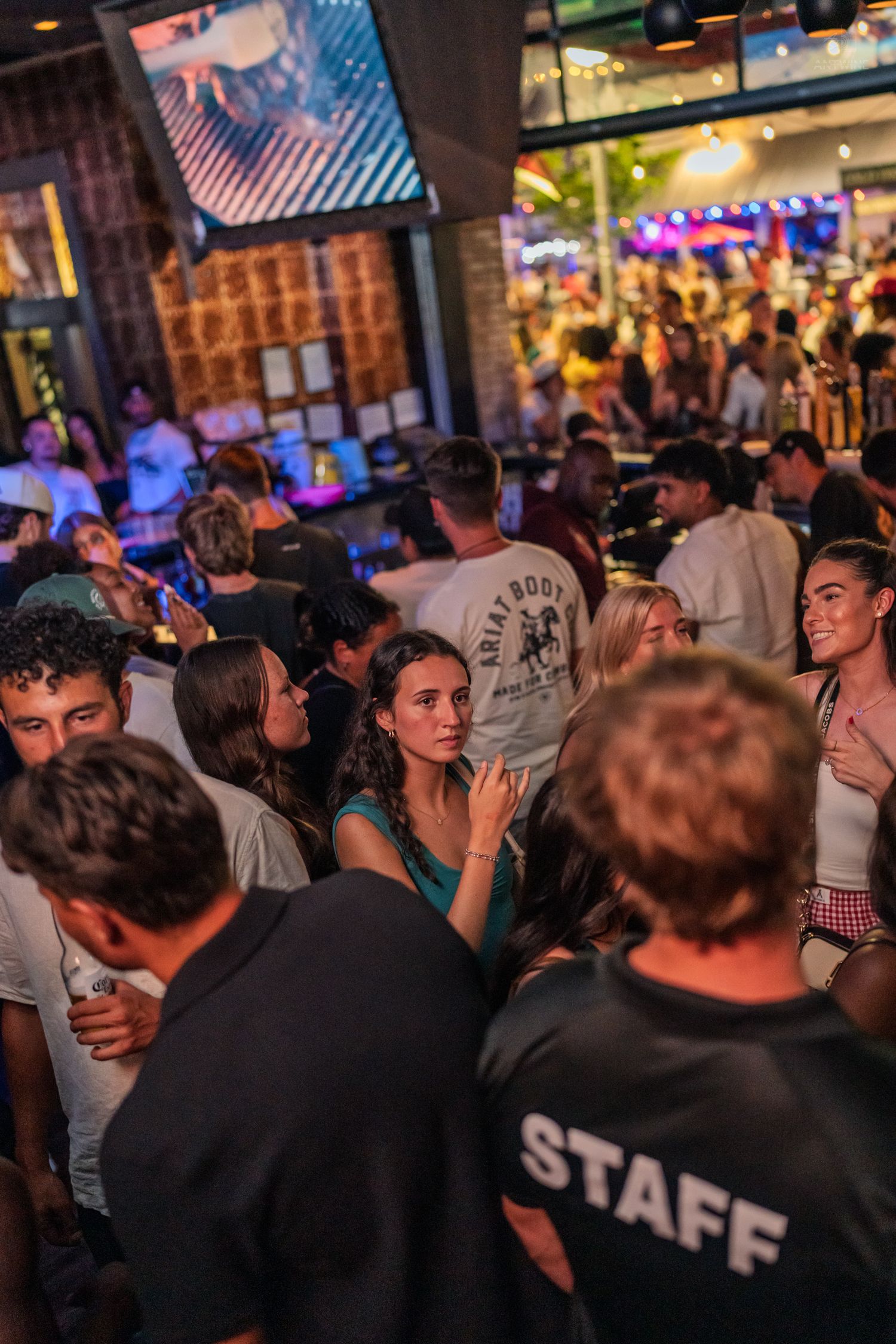 Crowded bar event with staff member in black shirt managing a lively nightlife crowd.