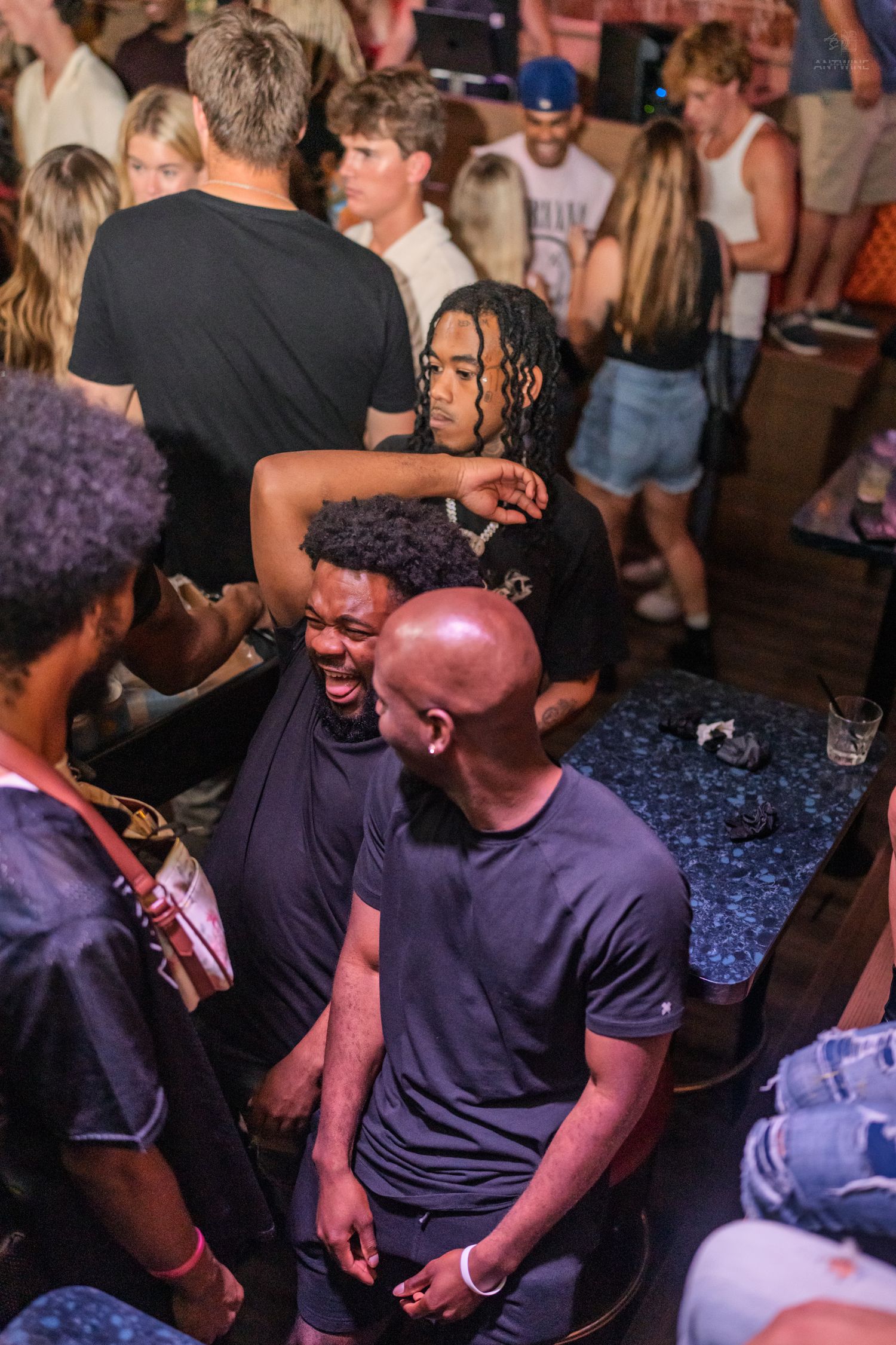 Group of friends laughing and socializing at a lively indoor bar or nightclub event.