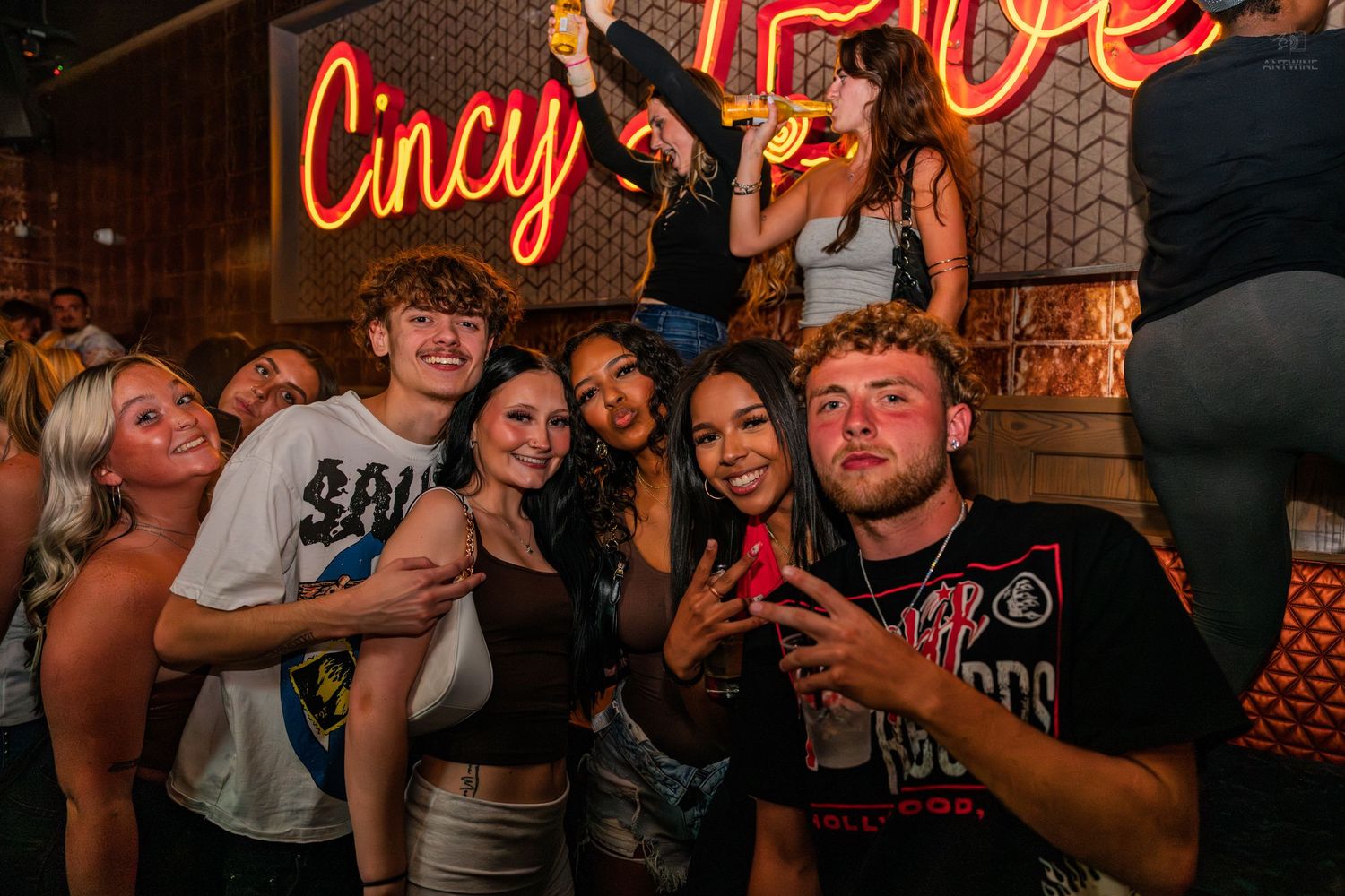 Group of young friends posing together at Cincy Love neon sign nightclub.
