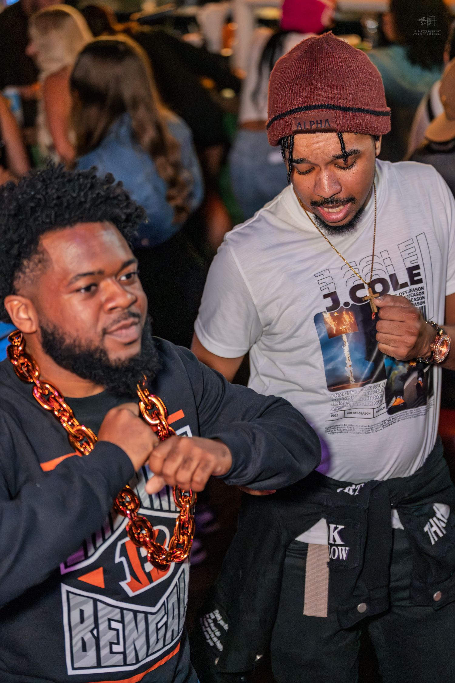Two men in a Cincinnati Bengals jersey and J. Cole shirt posing with fist bumps at a bar.