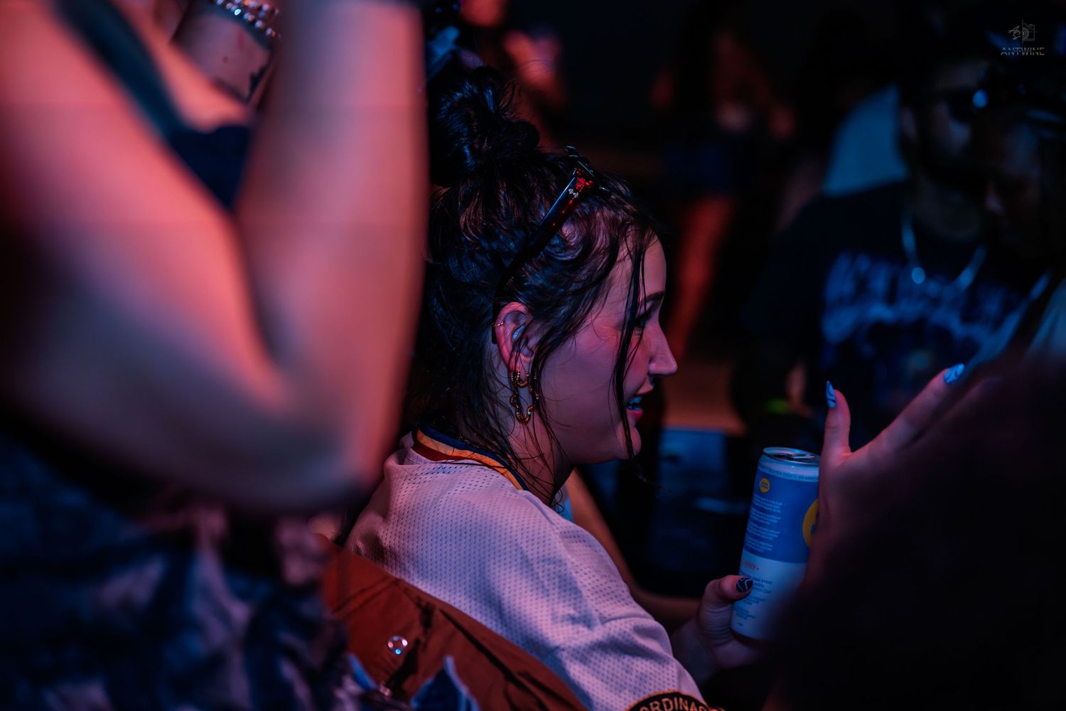 Young woman with wet hair holding drink can at crowded nighttime event.