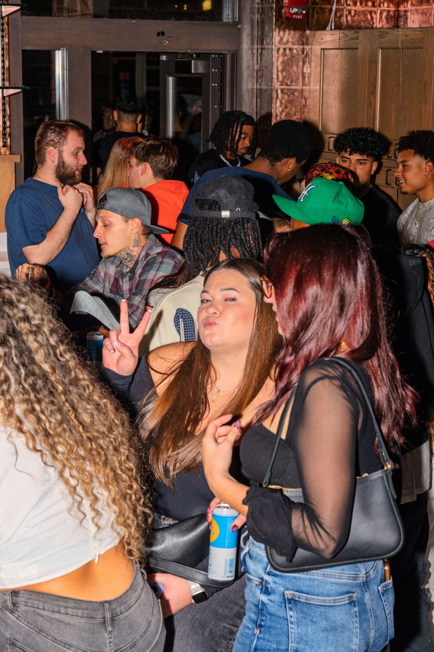 Young woman flashing peace sign while waiting in line outside a busy nightclub.