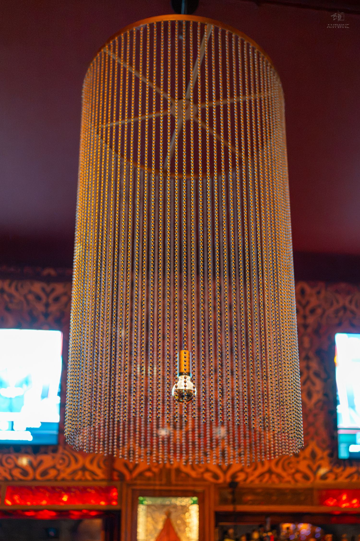 Elegant cylindrical chandelier with cascading gold beaded strands hanging from ornate ceiling in decorative interior.