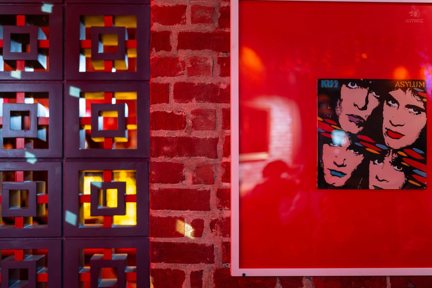 Red brick wall with colorful geometric screen divider and framed pop art portrait print in vibrant red tones.