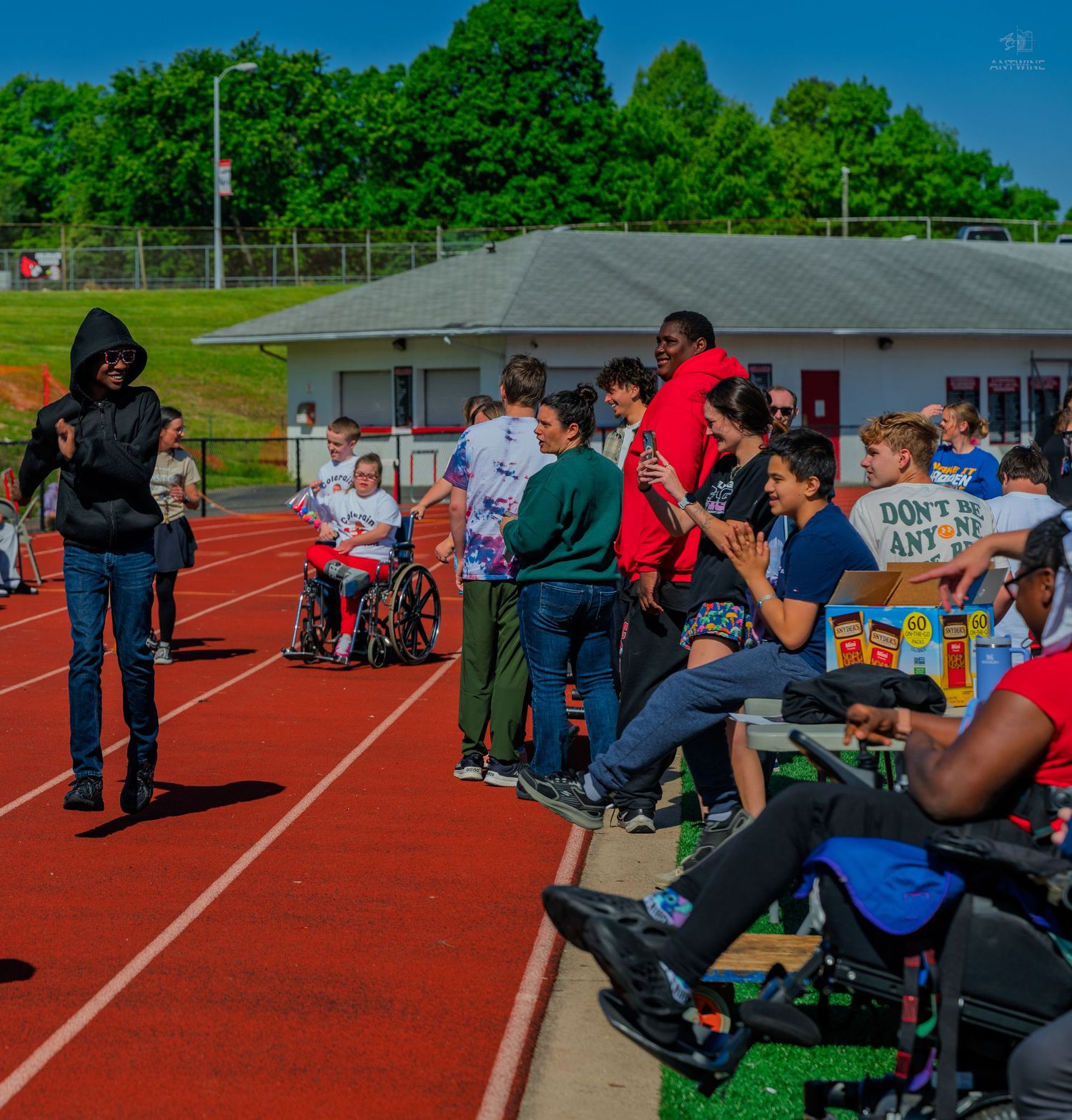 Students and teachers gather on a school running track during an inclusive outdoor sports event with wheelchair participants.