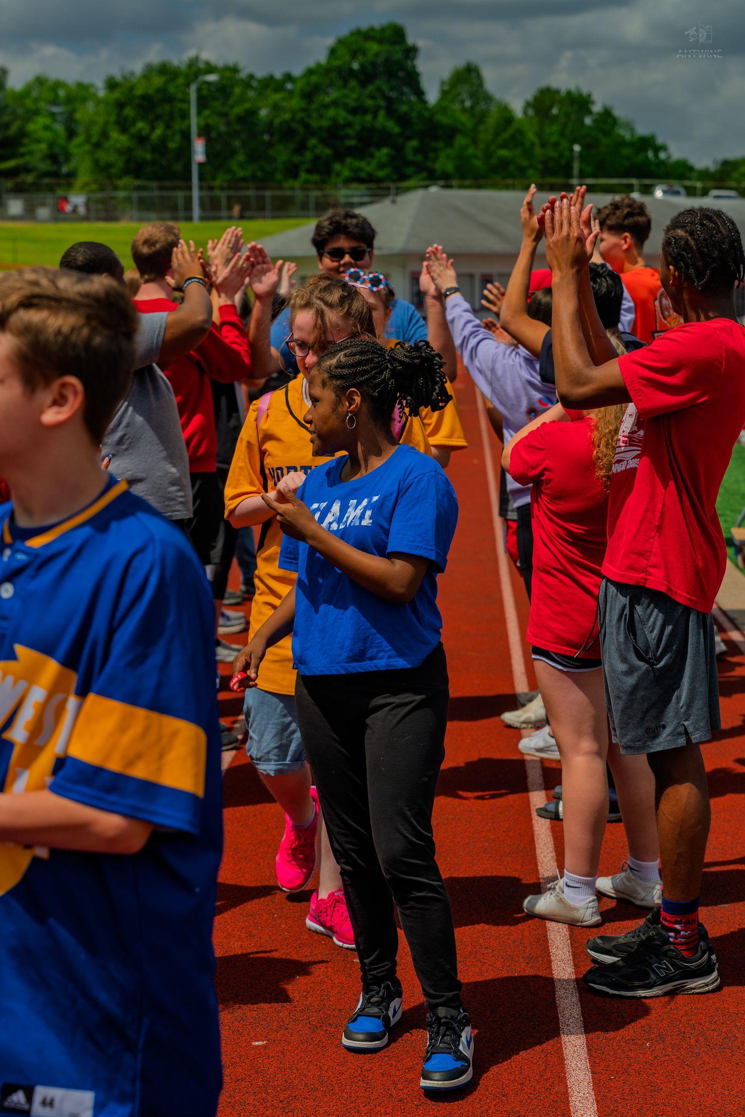 Students high-fiving on a track during an outdoor school sports event on a cloudy day.