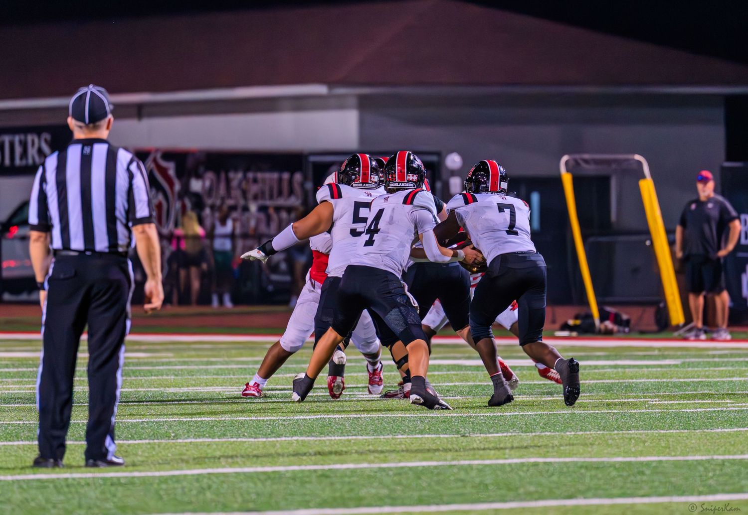 Colerain football players in red uniforms line up at scrimmage during a night game.