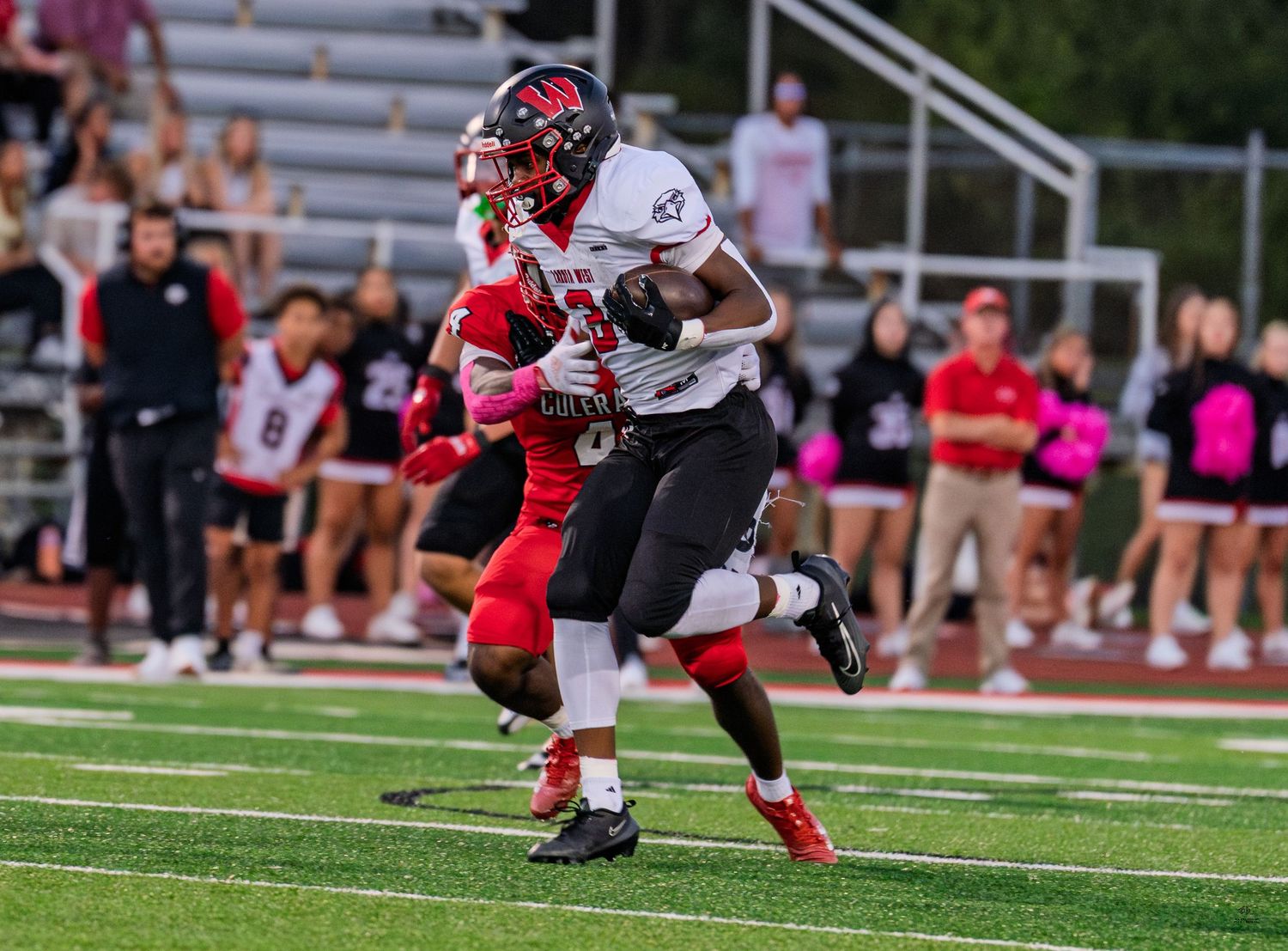 A wide receiver in white catches a pass while being defended during a high school football game.