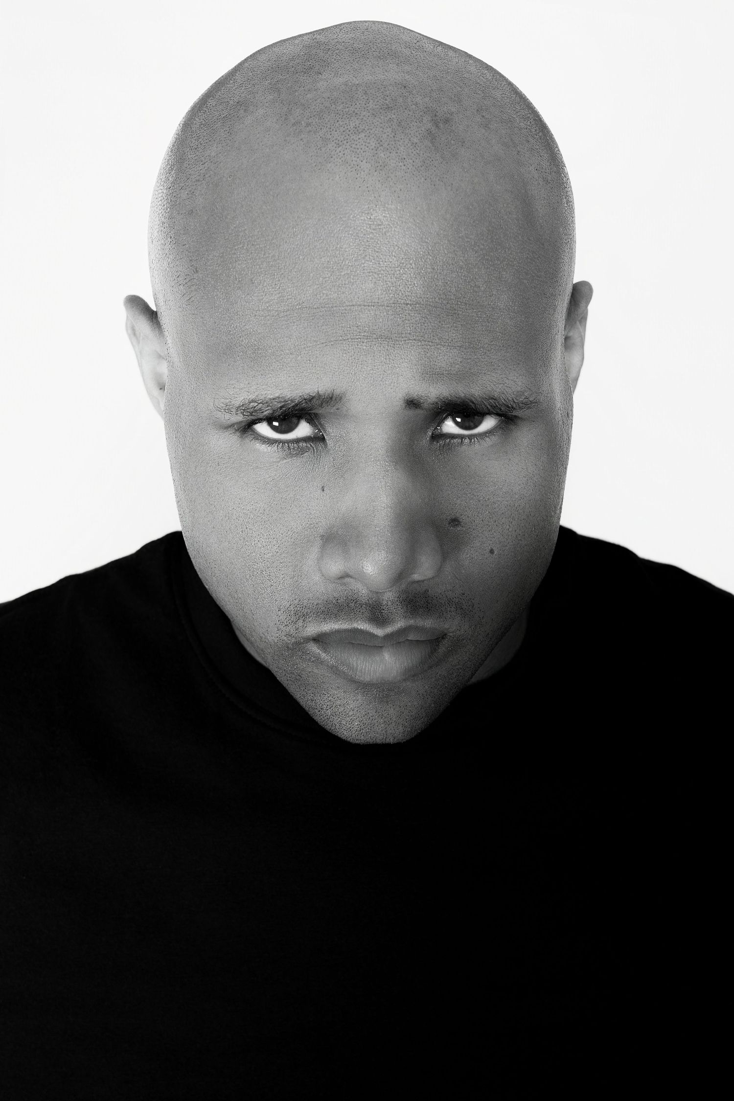 Close-up black and white portrait of bald man with intense expression in black t-shirt.