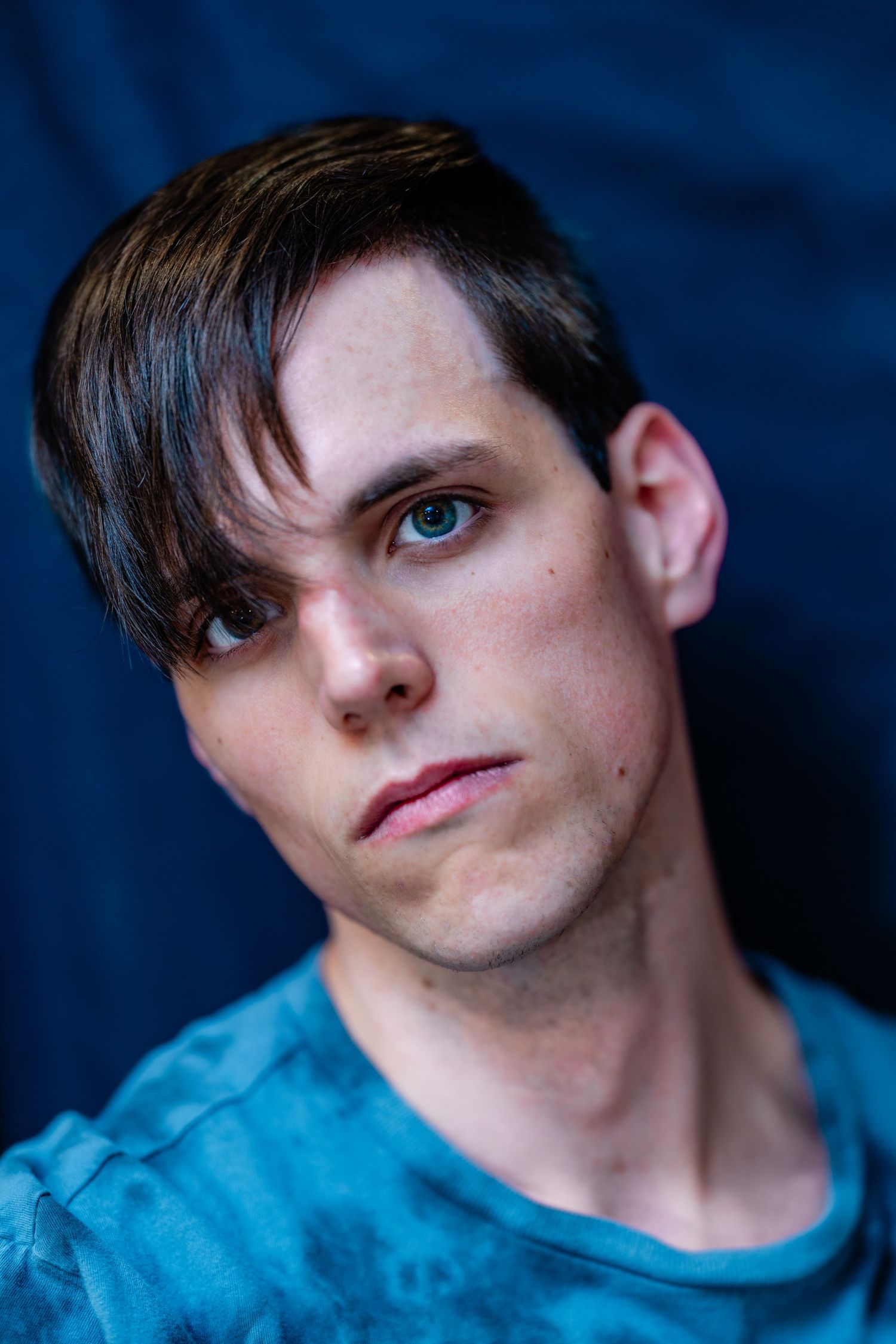 Young man in blue tie-dye shirt with dark swept hair against blue background.