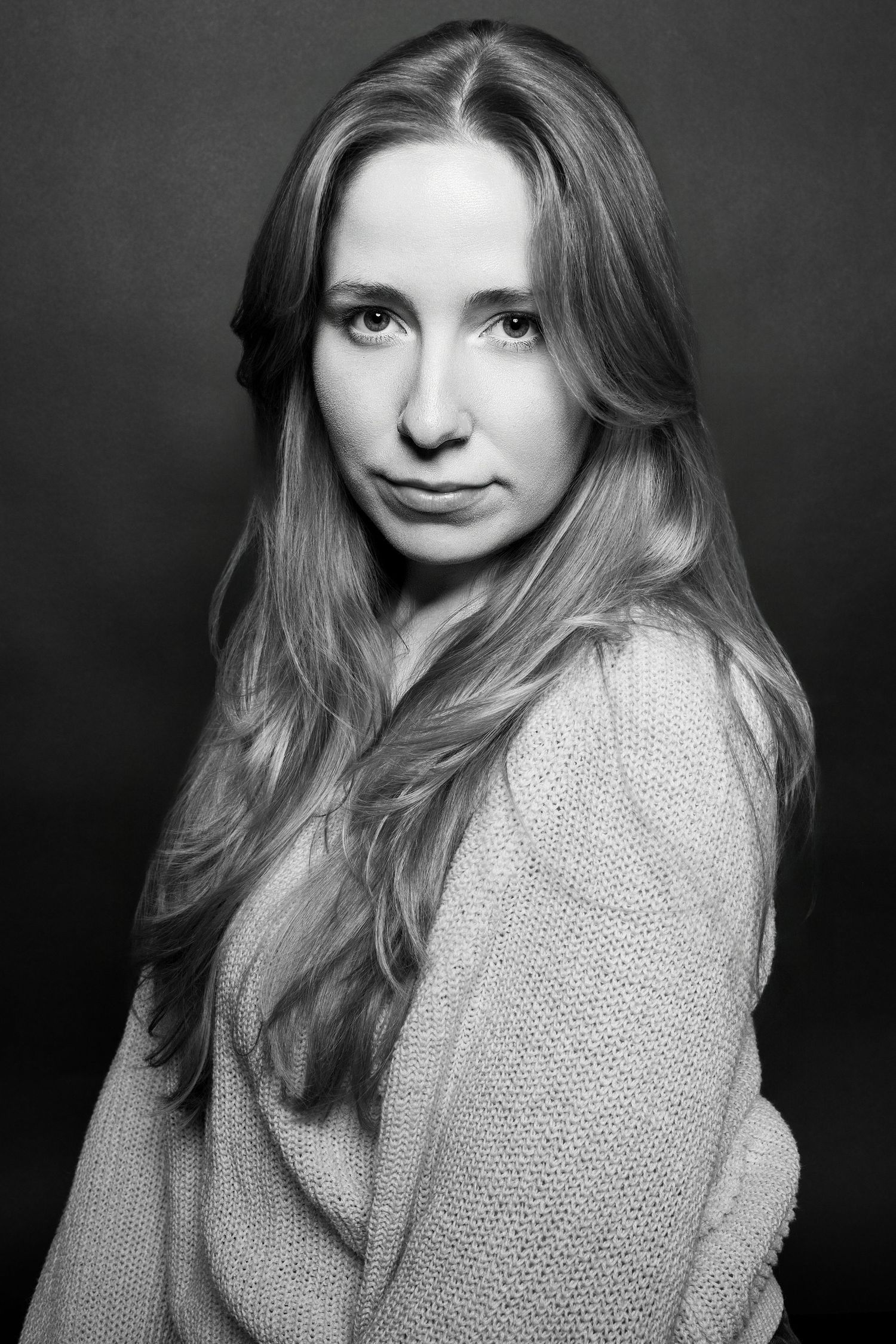 Black and white close-up portrait of a woman with long hair in a knit sweater, serious expression.