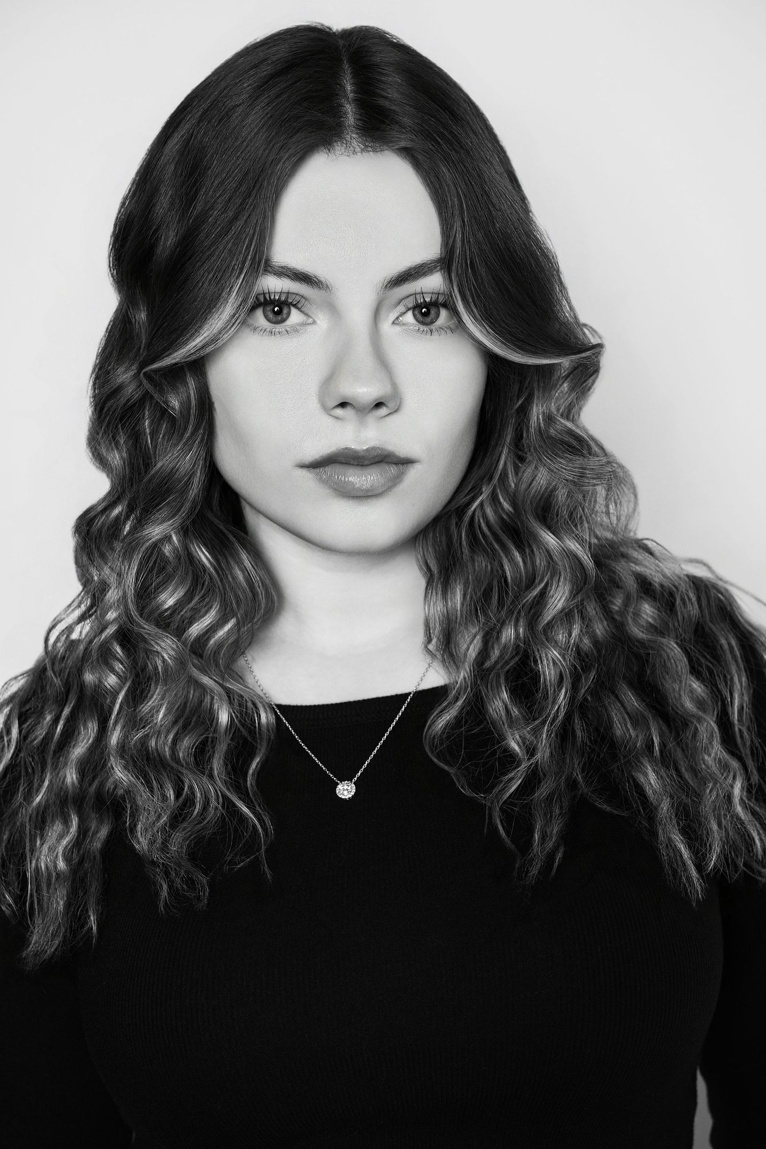 Black and white headshot of a young woman with voluminous curly hair wearing a black top.