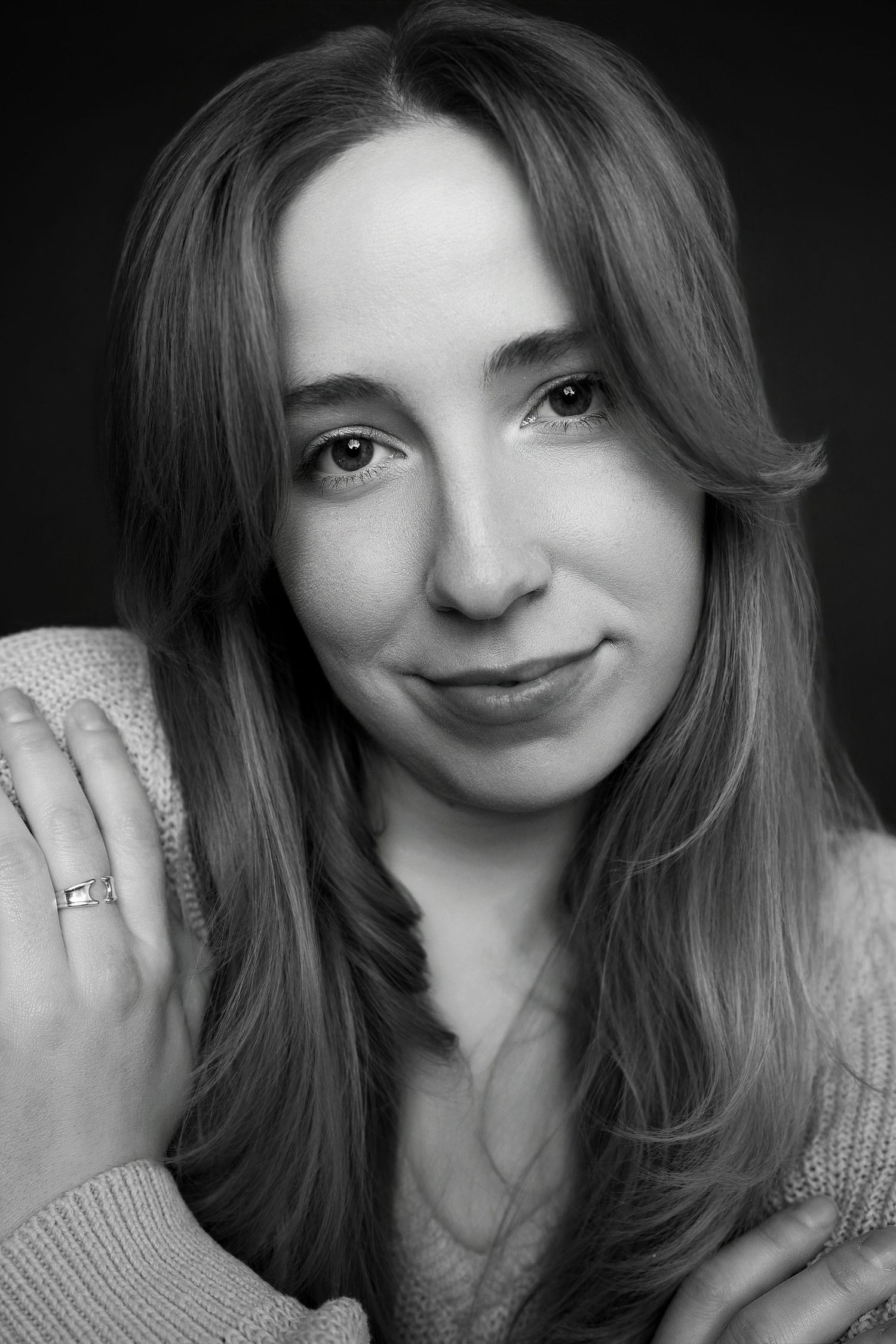 Black and white portrait of young woman in knit sweater with ring, smiling softly at camera.