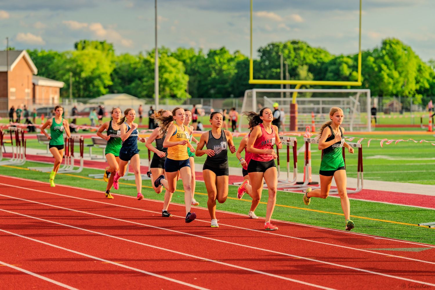 Group of female athletes run together during outdoor high school track meet.