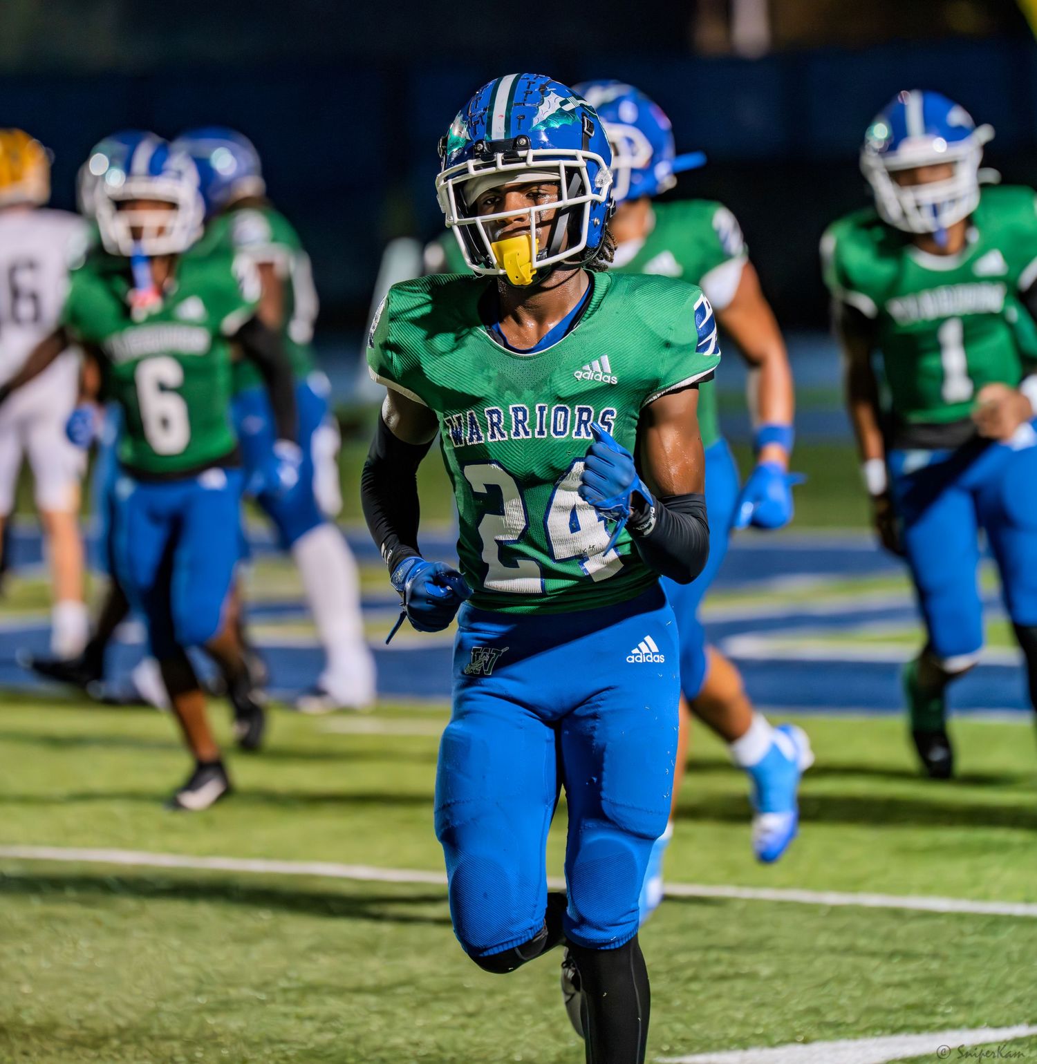 Warriors football player number 24 in green jersey sprints down the field during a night game.