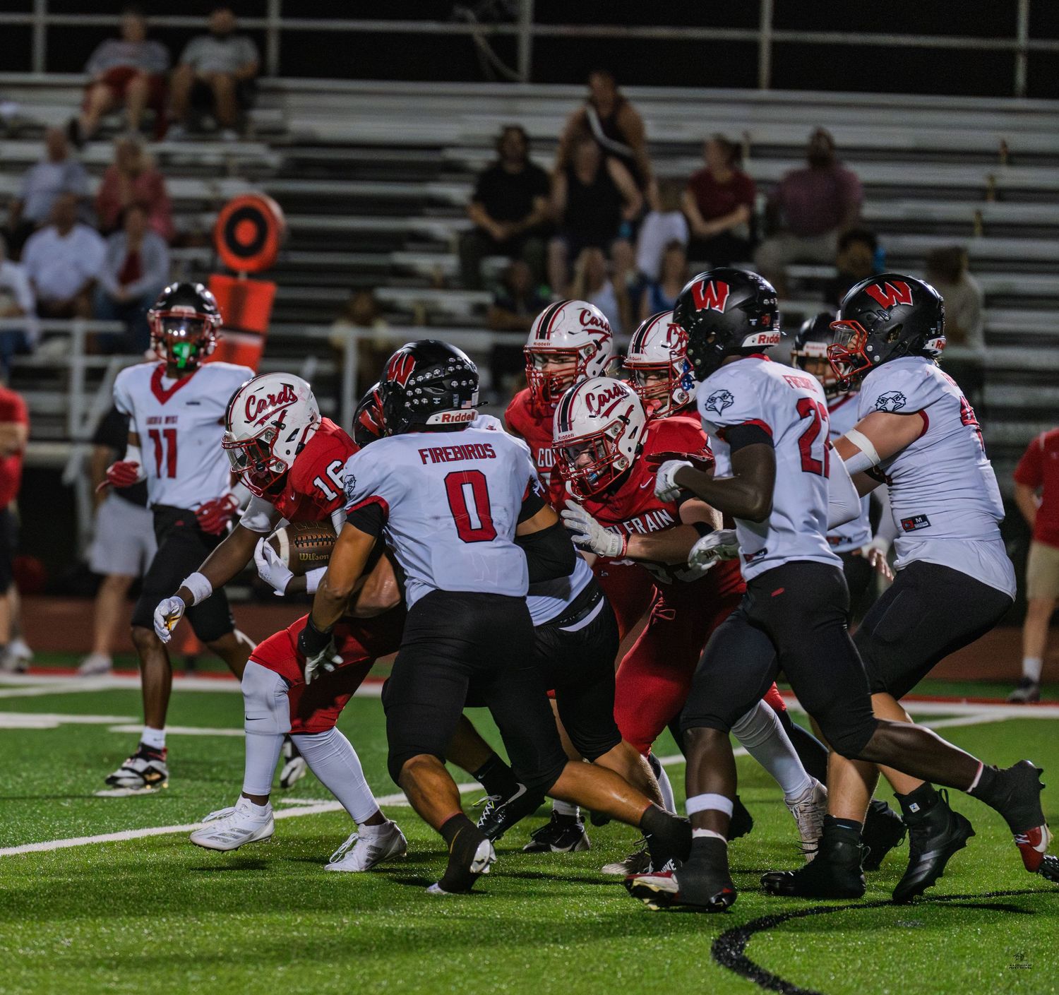 Red and white-uniformed football players collide in a intense line scrimmage during a high school game.