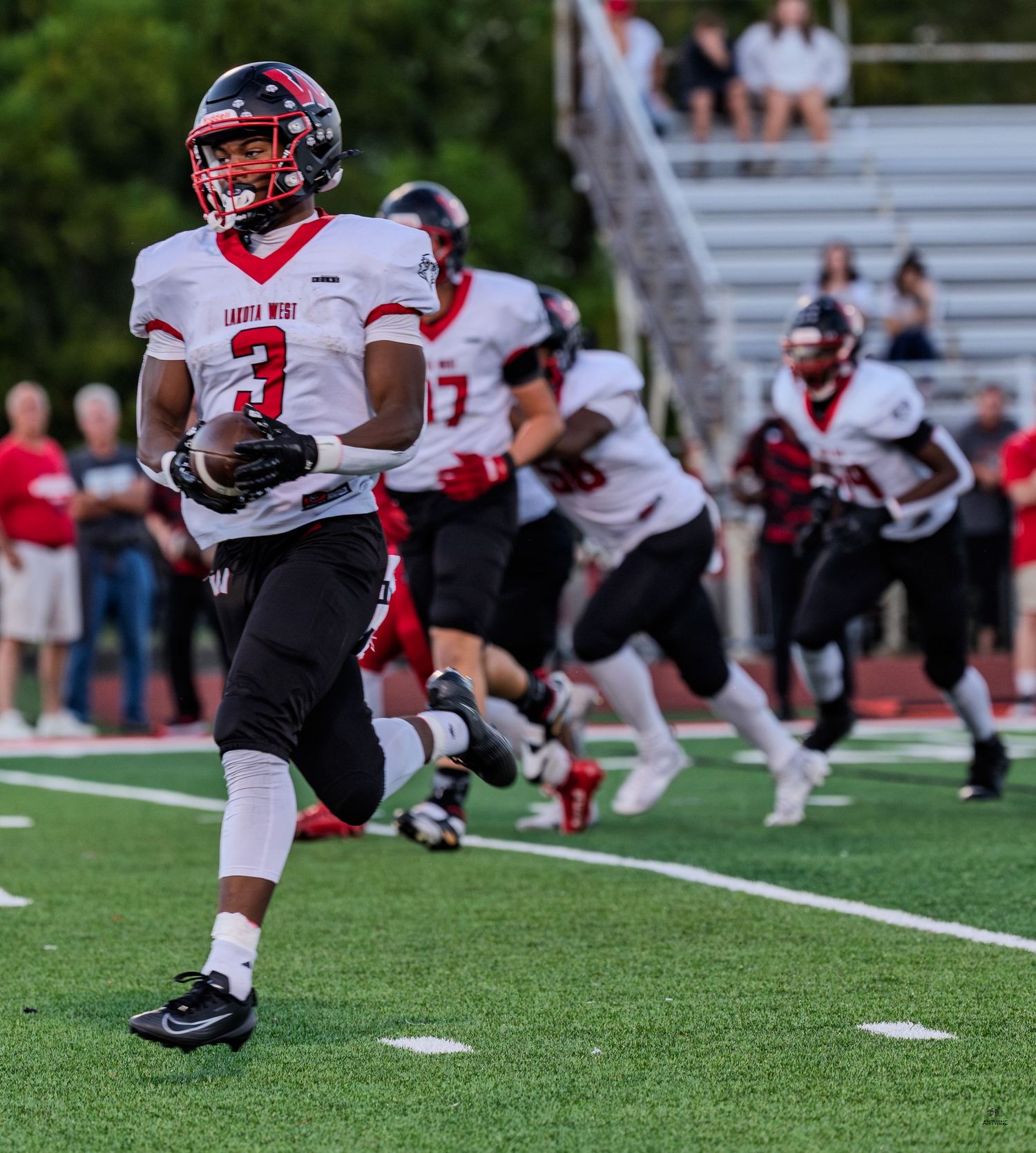A football player wearing number 3 runs with the ball during a high school football game.