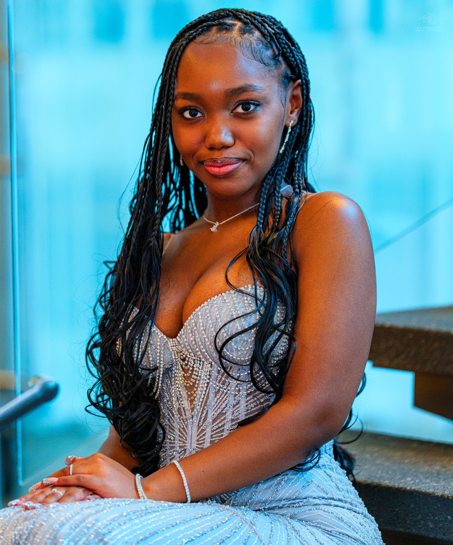 Young woman with long box braids wearing silver beaded gown at formal event.