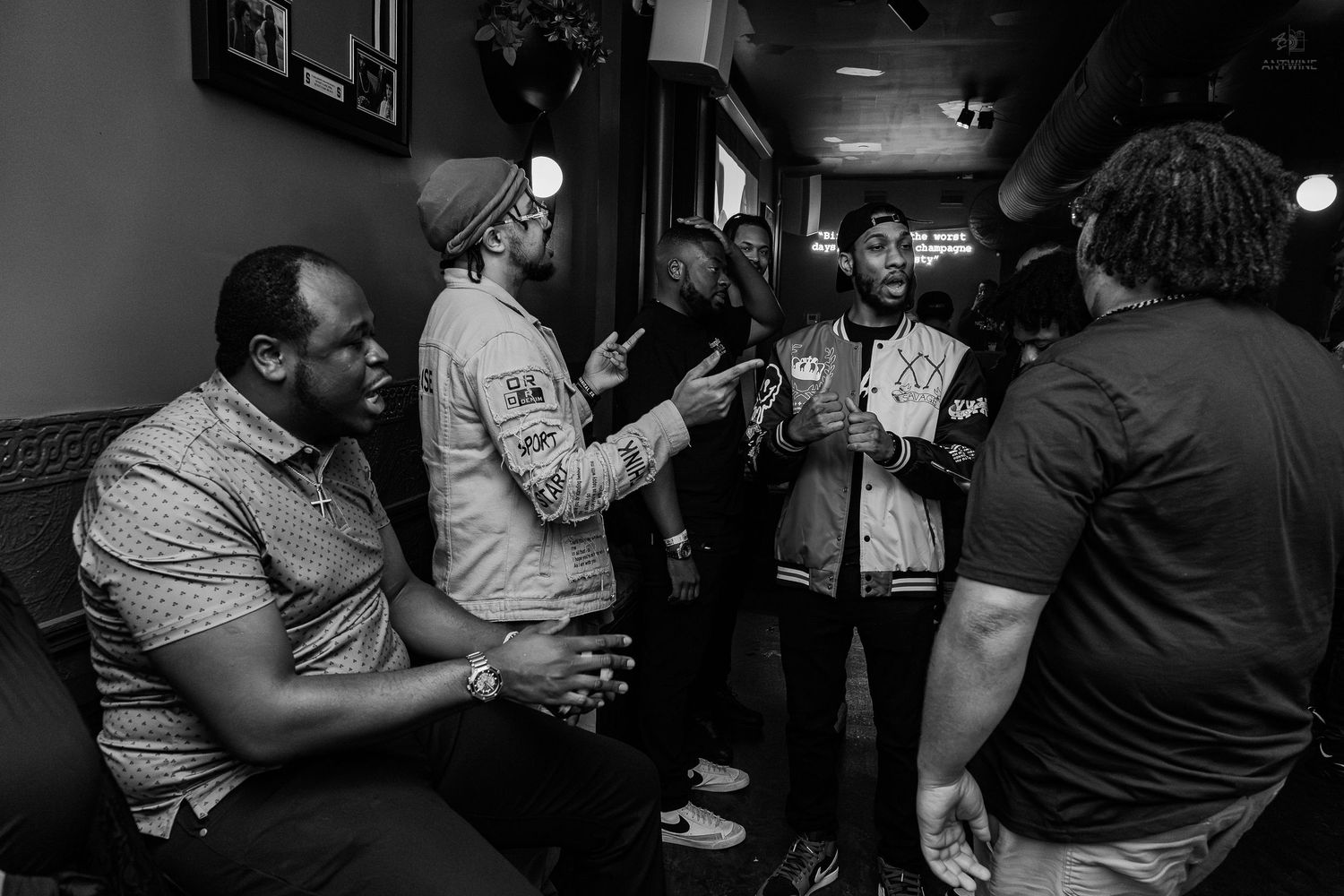 Black and white photo of a group of men socializing and conversing in a dimly lit bar or lounge.