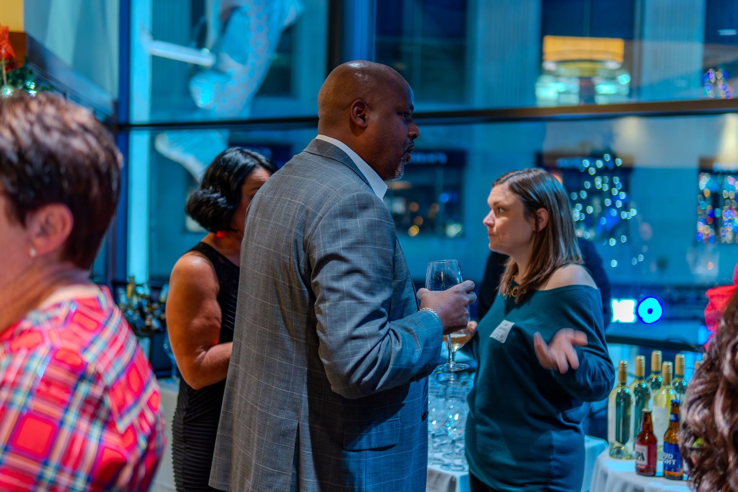 Professionals networking at an indoor corporate cocktail party, holding drinks and engaging in conversation.