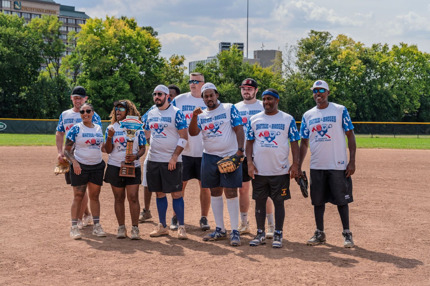 Group of nine softball players pose together on a baseball diamond at the Battle of the Badges charity game.