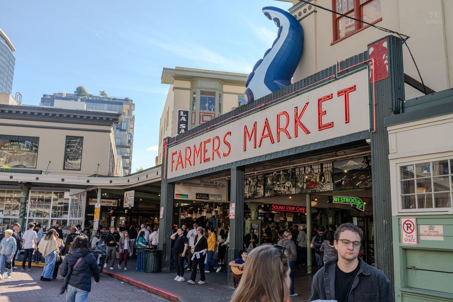 Crowds gather outside Pike Place Farmers Market in Seattle on a sunny day.