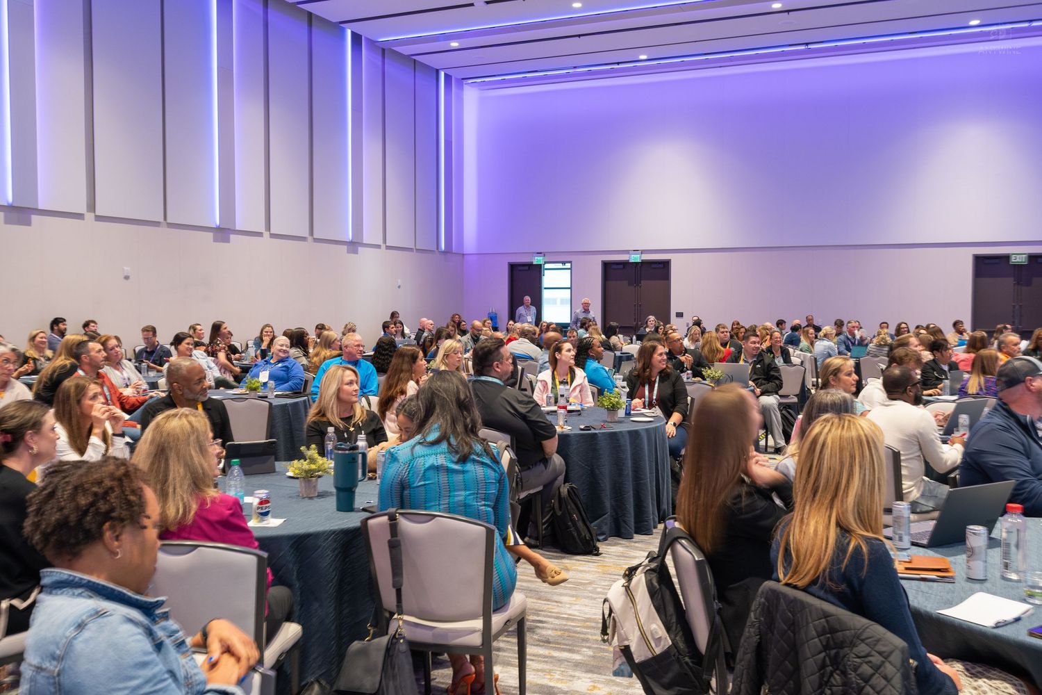 Large conference ballroom filled with hundreds of attendees seated at round tables during a professional event.