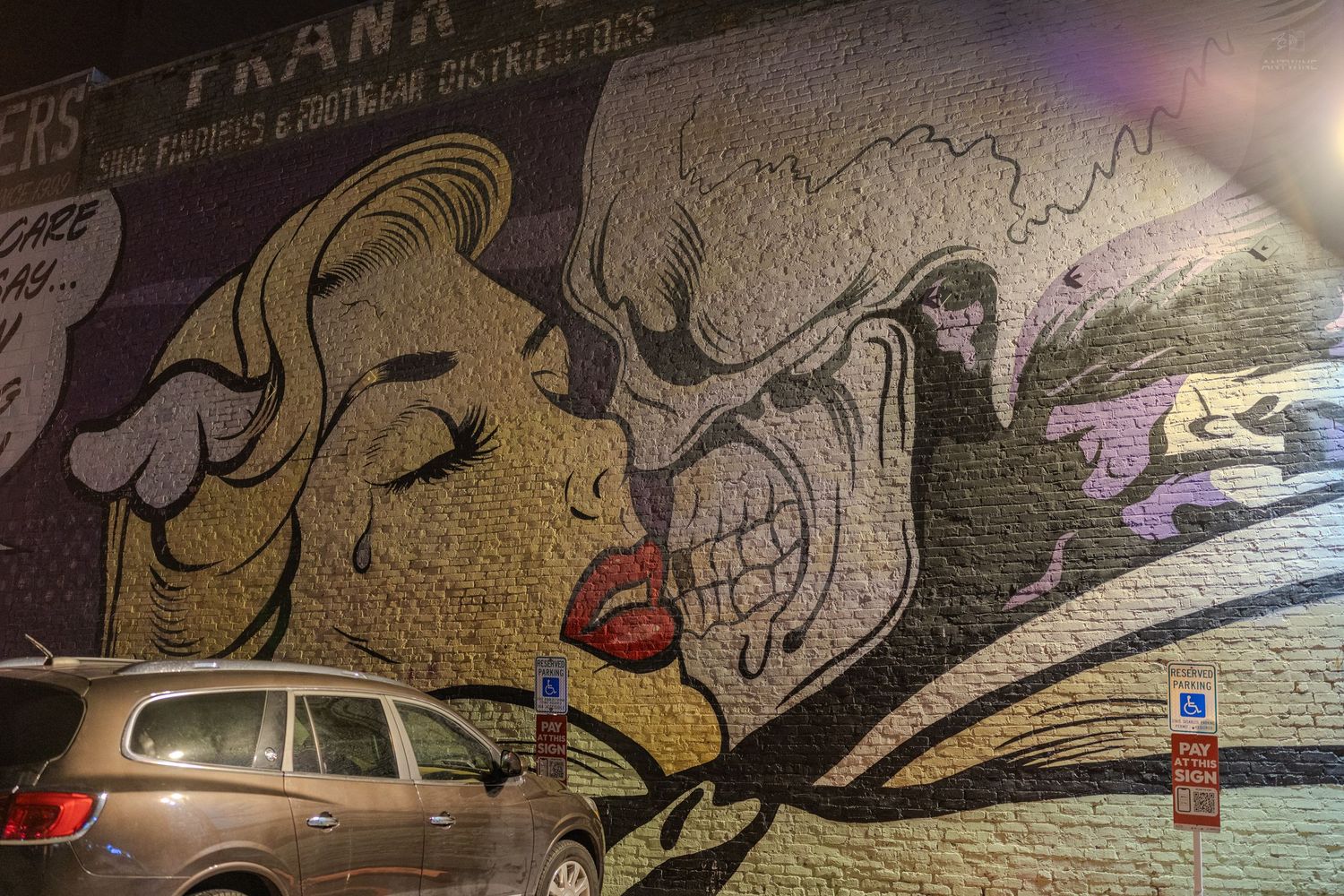 Vibrant street art mural on brick wall featuring pop-art style faces with bold colors at night.