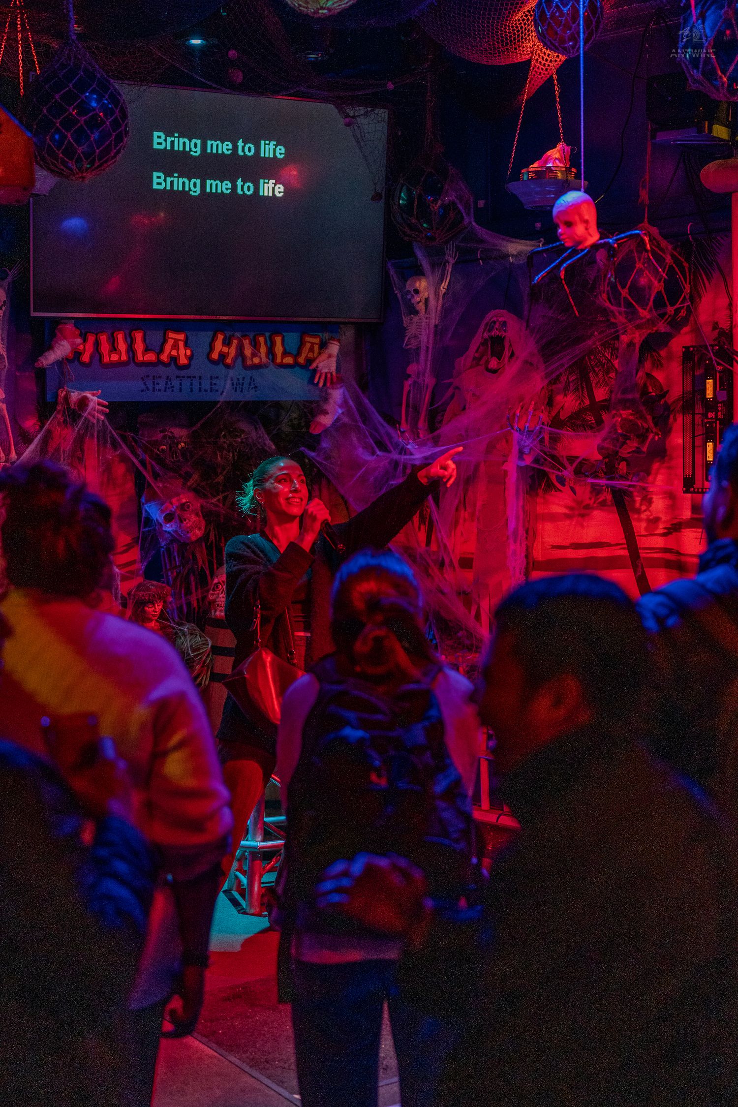Halloween karaoke night at Hula Hula bar with colorful lights, spiderwebs, and a performer singing Bring Me to Life.