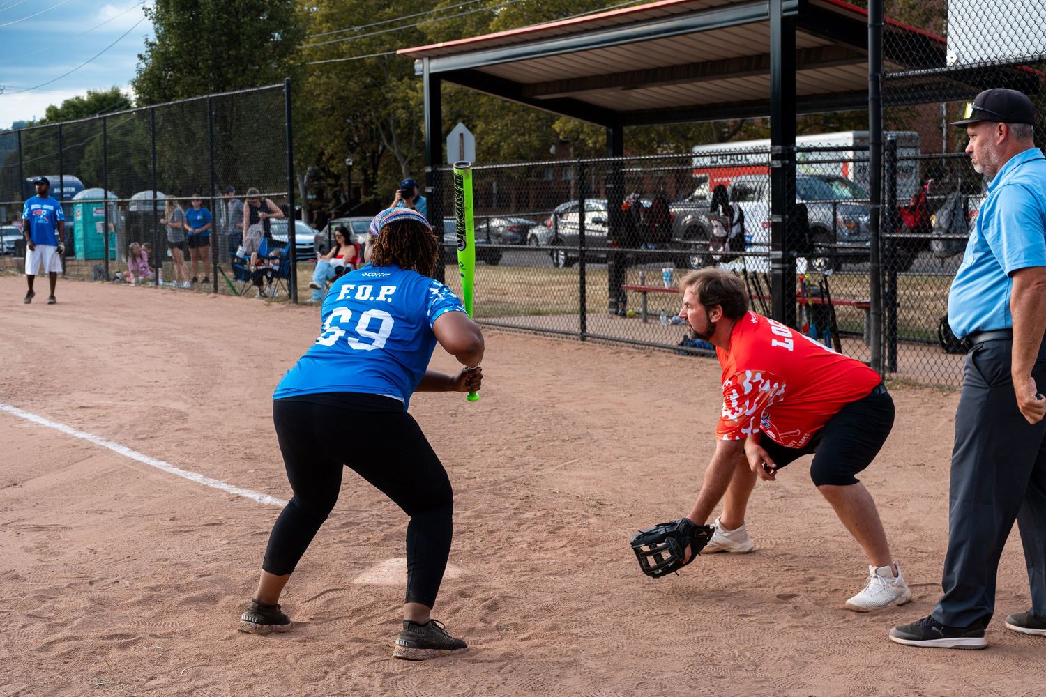 Softball player in blue jersey number 69 prepares to field a ball during a recreational league game on a dirt diamond.