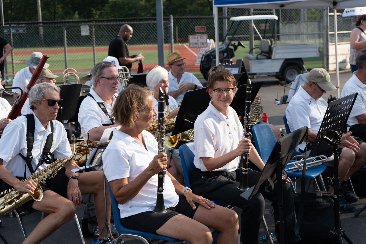Outdoor band concert featuring musicians playing saxophones and clarinets in white shirts at a summer event.