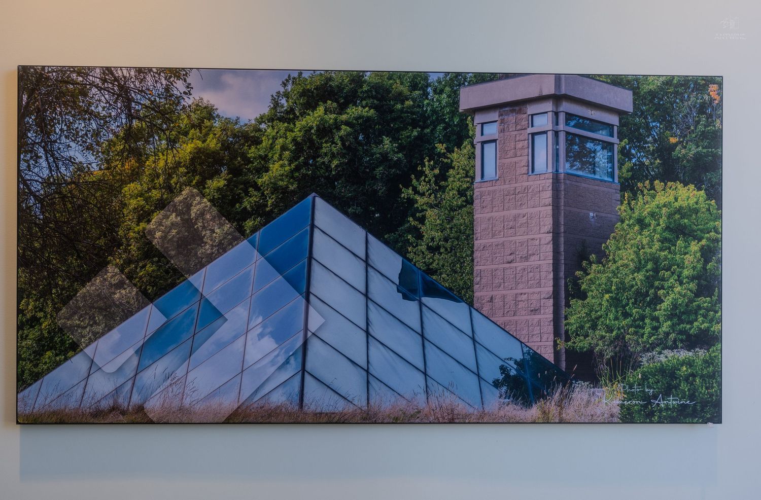 Canvas print of a glass pyramid structure beside a brick tower surrounded by lush green trees.